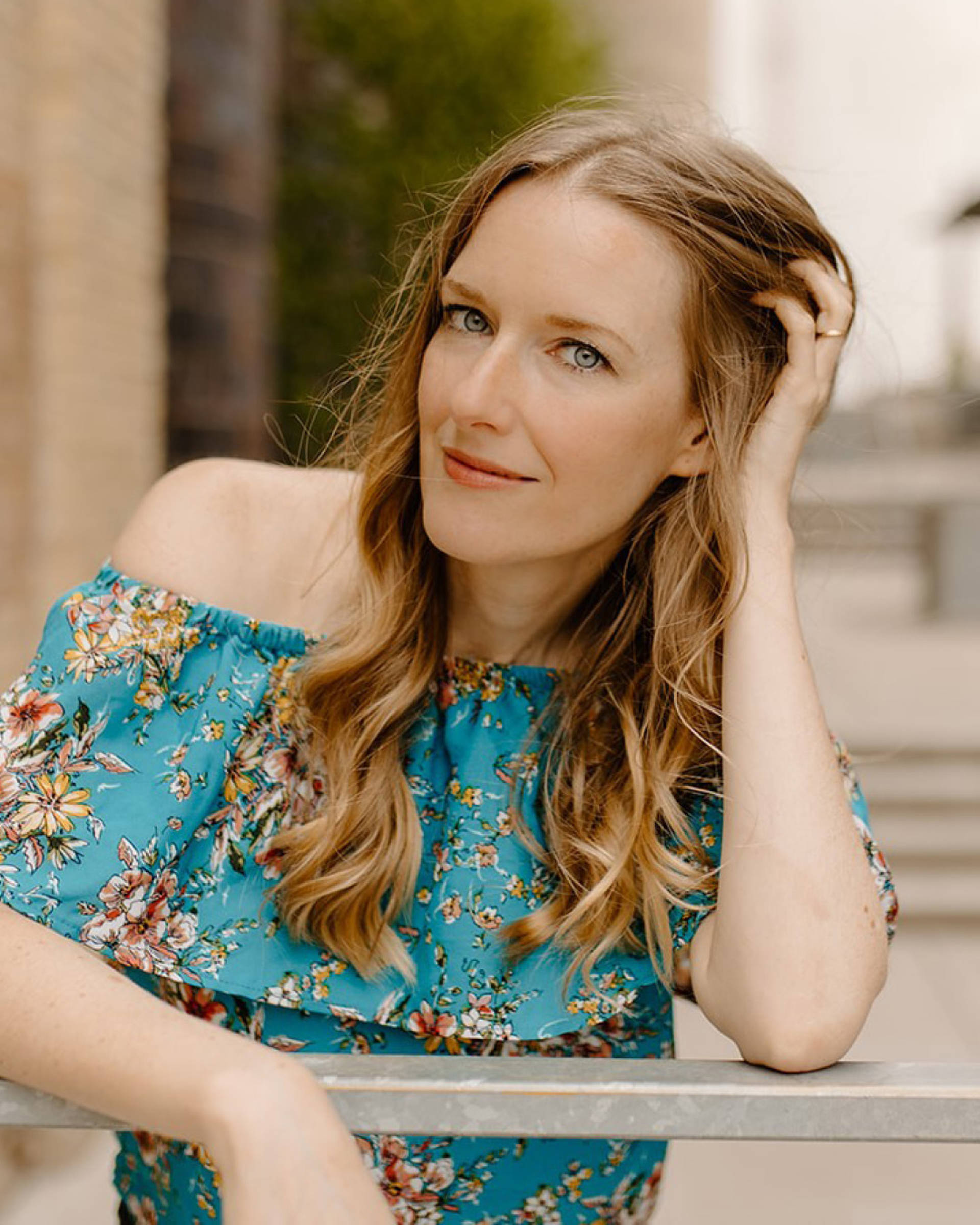Headshot of a caucasian woman with long dark blond hair, blue eyes and a blue top with floral pattern.
