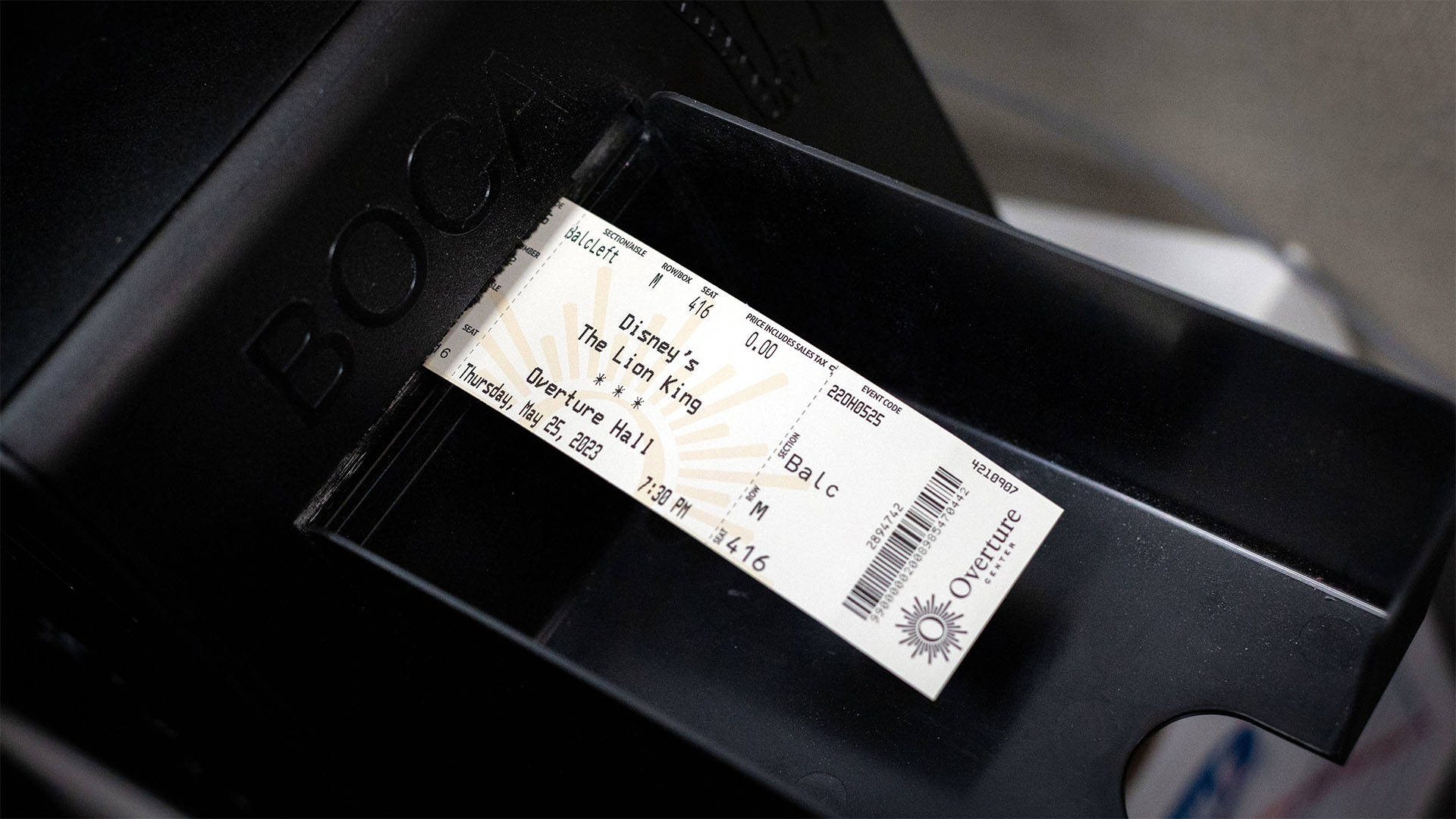 An Overture ticket being printed from a small black printer. The ticket says "Disney's The Lion King."