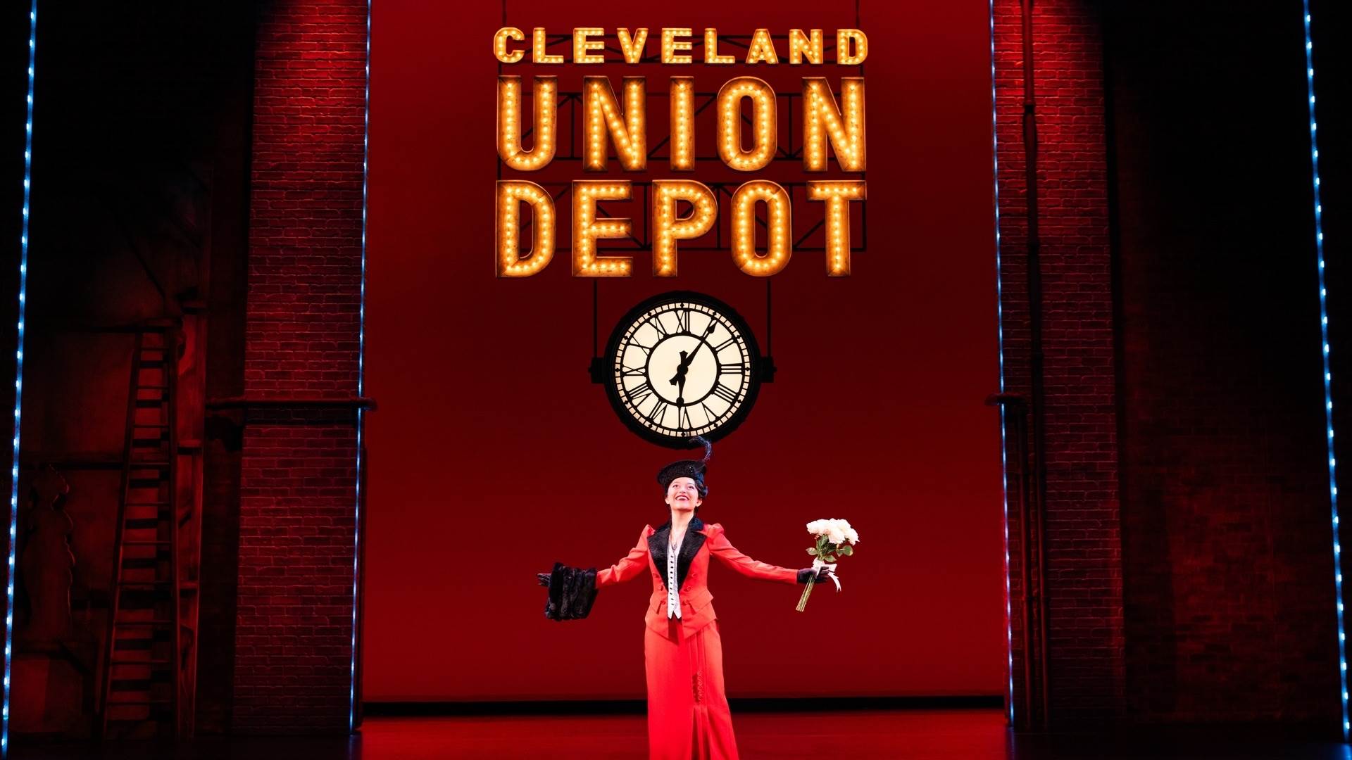 A woman in a red dress holding a bouquet of flowers under a clock and a sign that reads cleveland union depot.