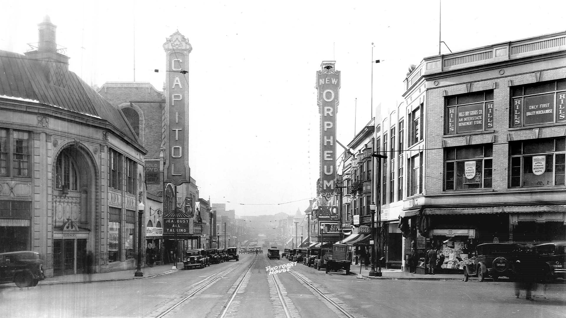 A black and white photo of State Street circa 1928. Two marquees stand vertically on each side of the street. On the left reads 'Capitol' and on the right .New Orpheum'.