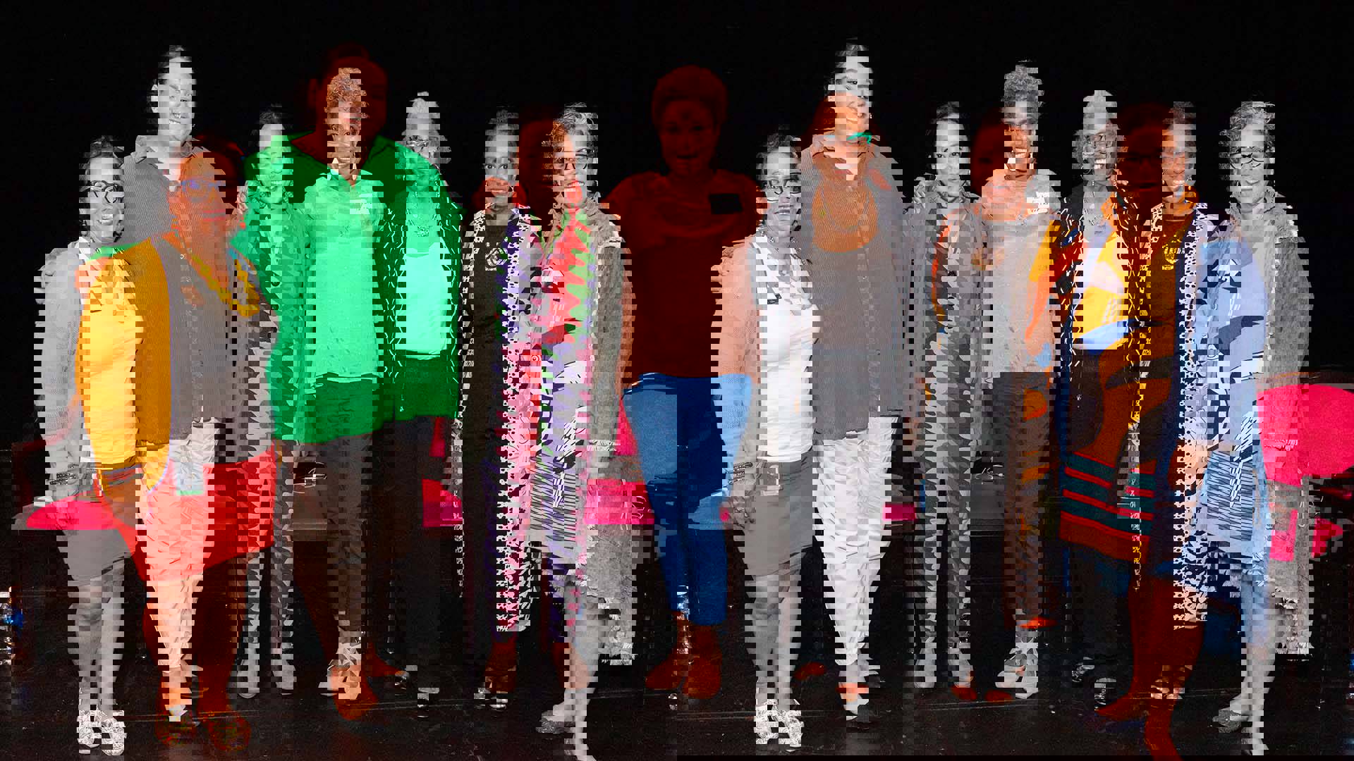 Seven women stand together for a photo on a dark stage.