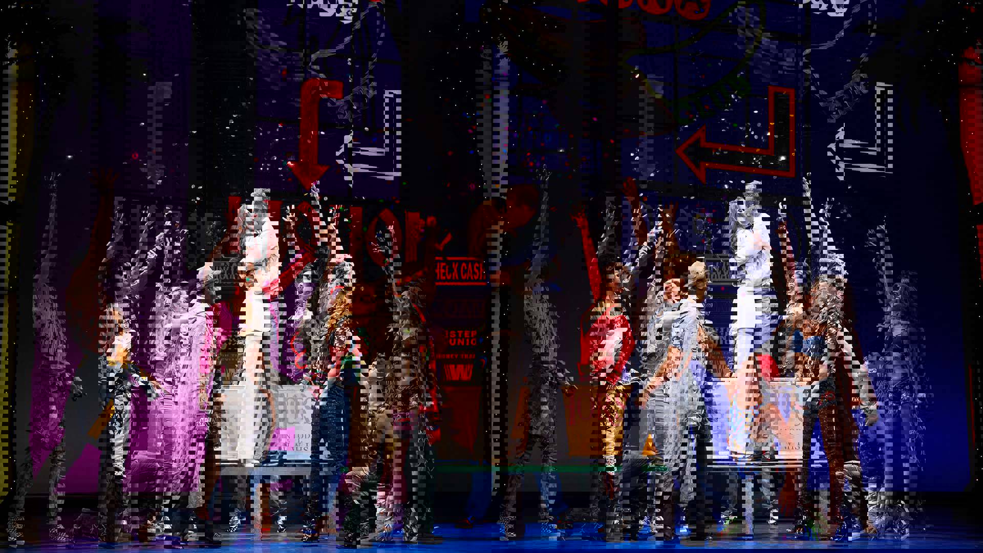The Cast of Pretty Woman performing on stage. Two people are kissing in the center.