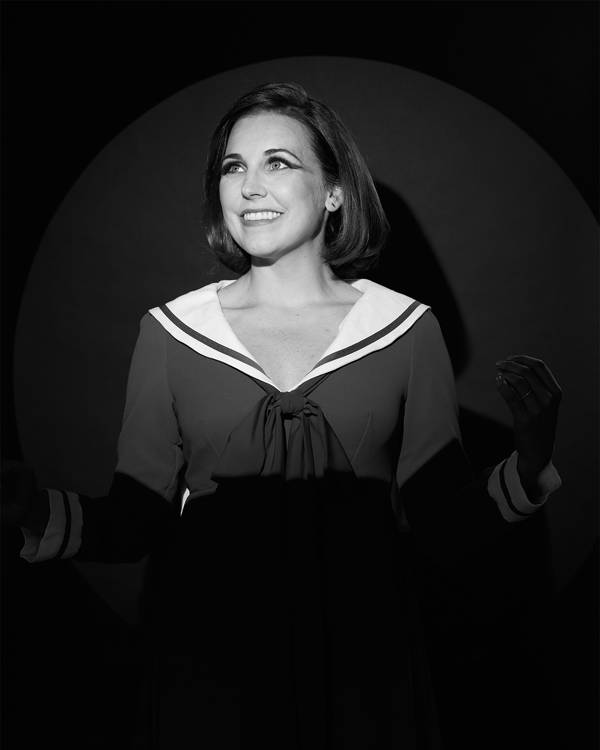 Greyscale headshot of a caucasian woman with medium hair smiling. She is wearing a top styled like a sailor outfit.