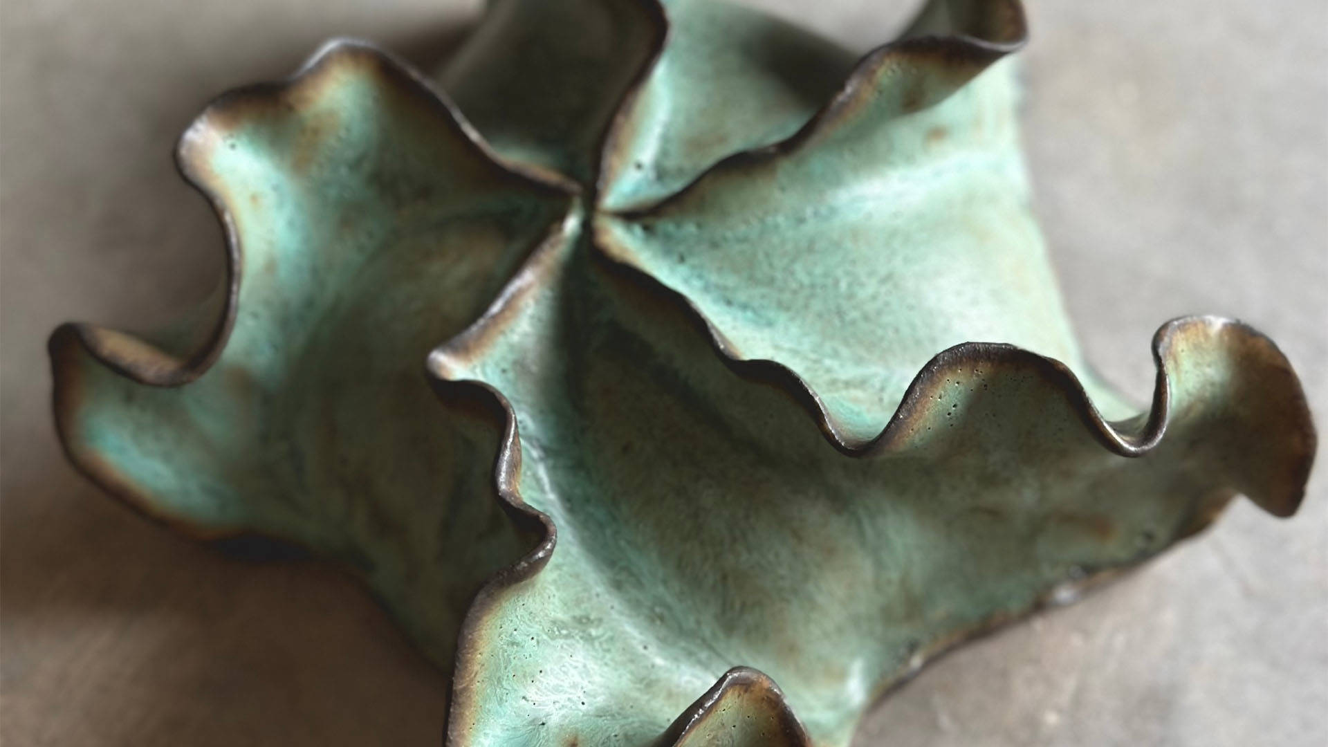 A green and brown ceramic sculpture with wavy components meeting in the center