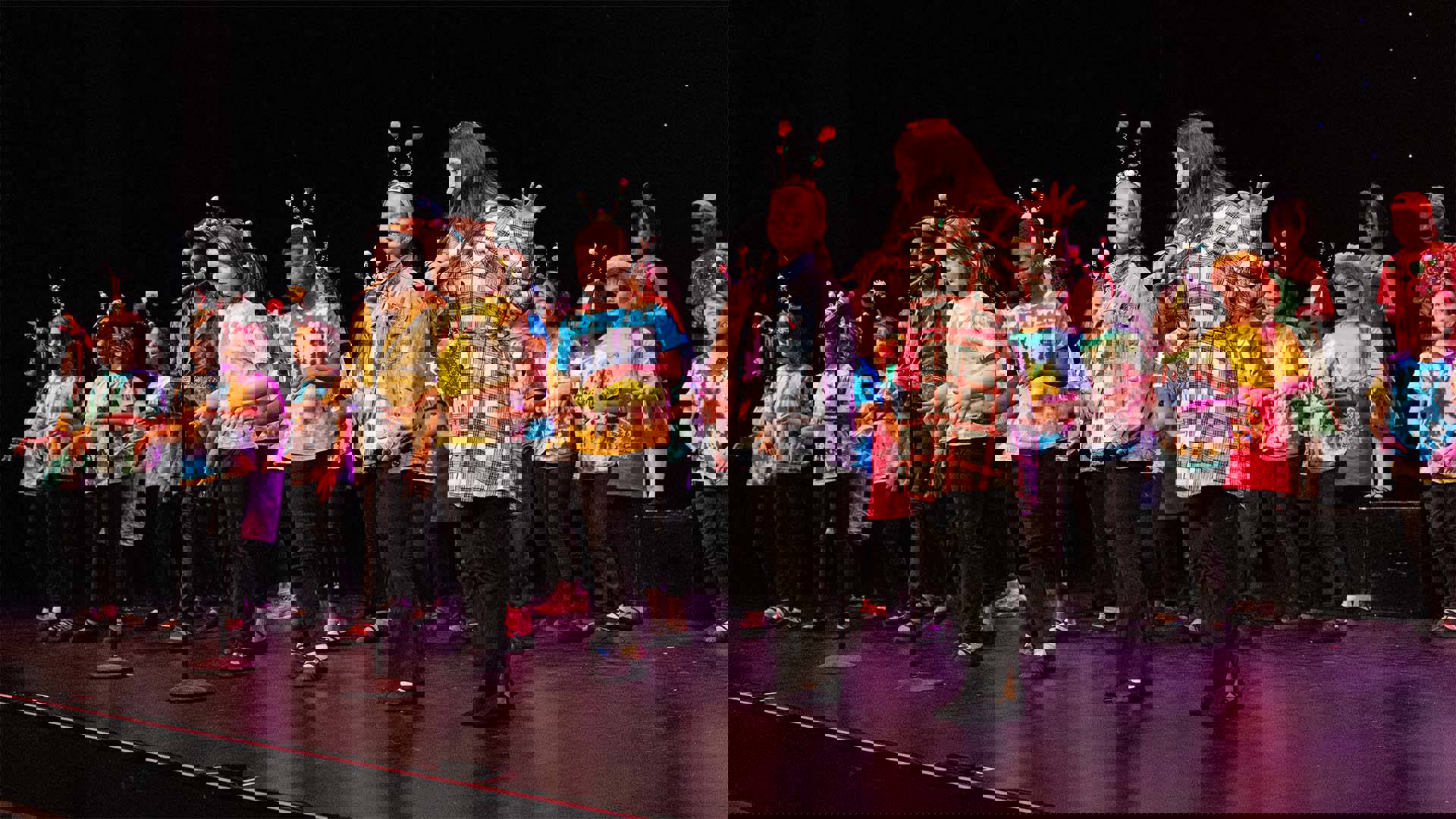 Young students in colorful clothing and cute instect antennae headwear performing on a dark stage. 
