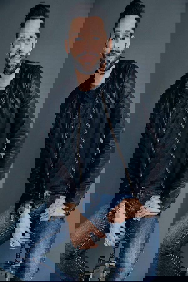 Headshot of Ryan Silverman. He has a handsome youthful face with short brown hair and brown eyes. He is wearing a leather jacket and T-shirt with jeans.