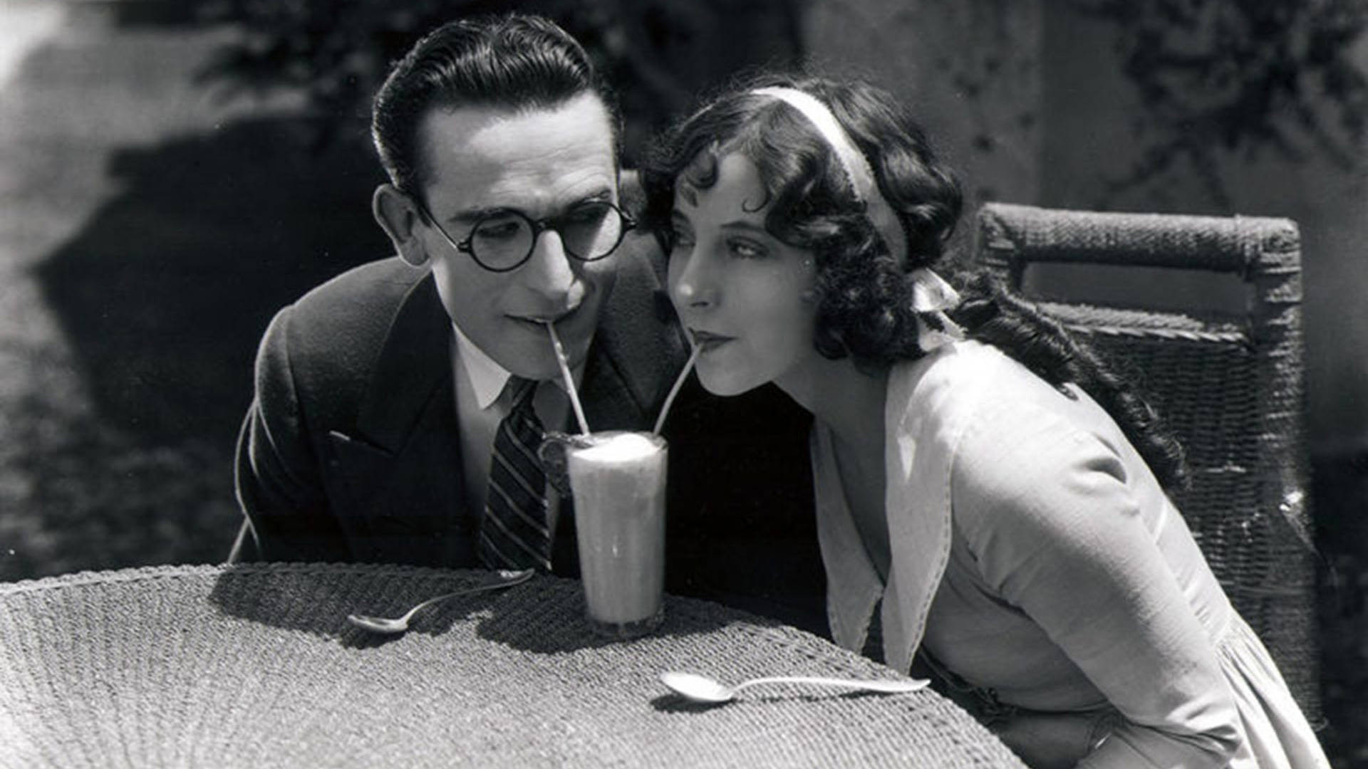 Light complexion man and woman sip on a milkshake using two straws in a scene from "For Heaven's Sake (1926)."