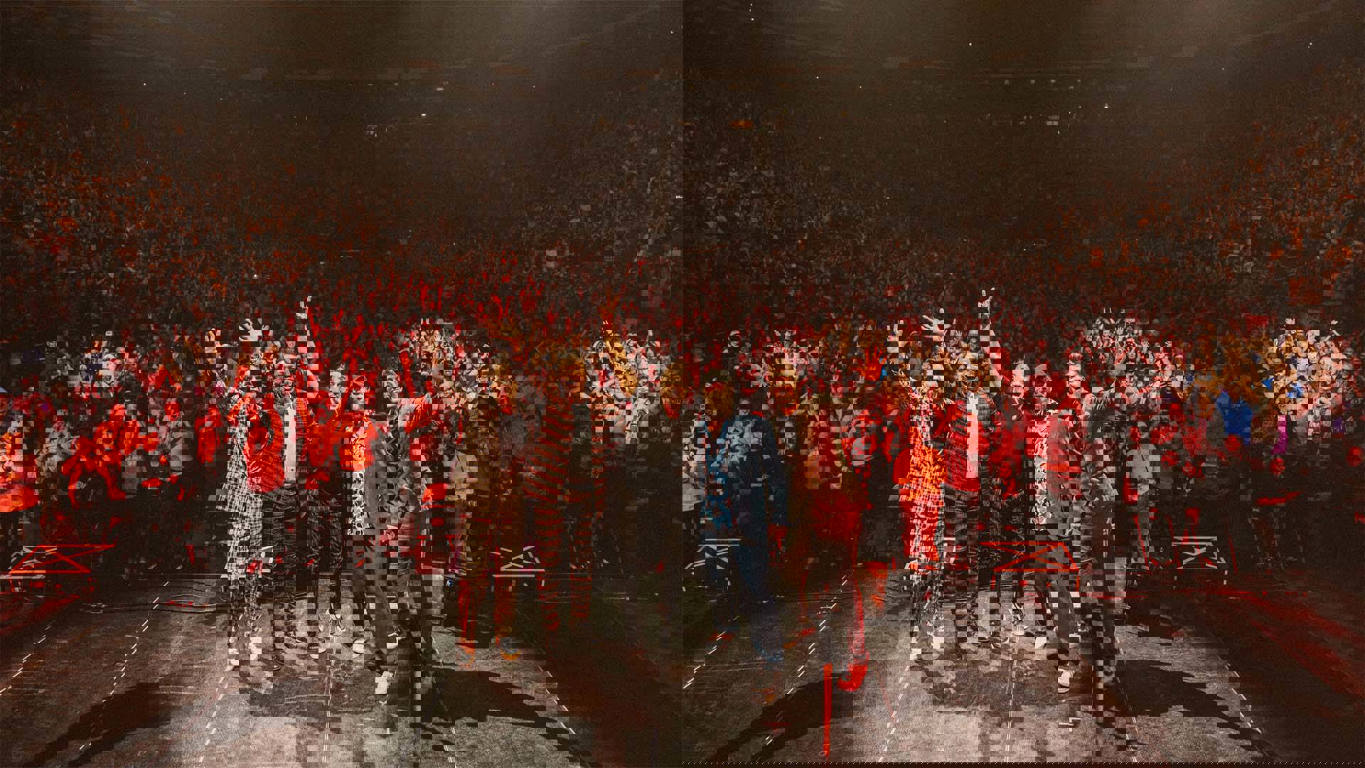 Five rock musicians posing for a photo together with a large crowd behind them.