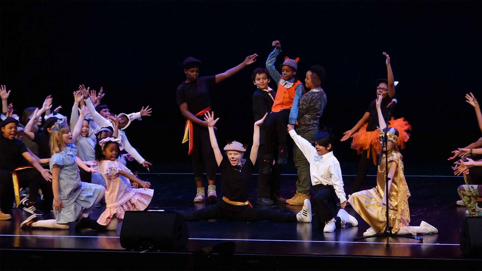A group of children in various costumes performing on stage.
