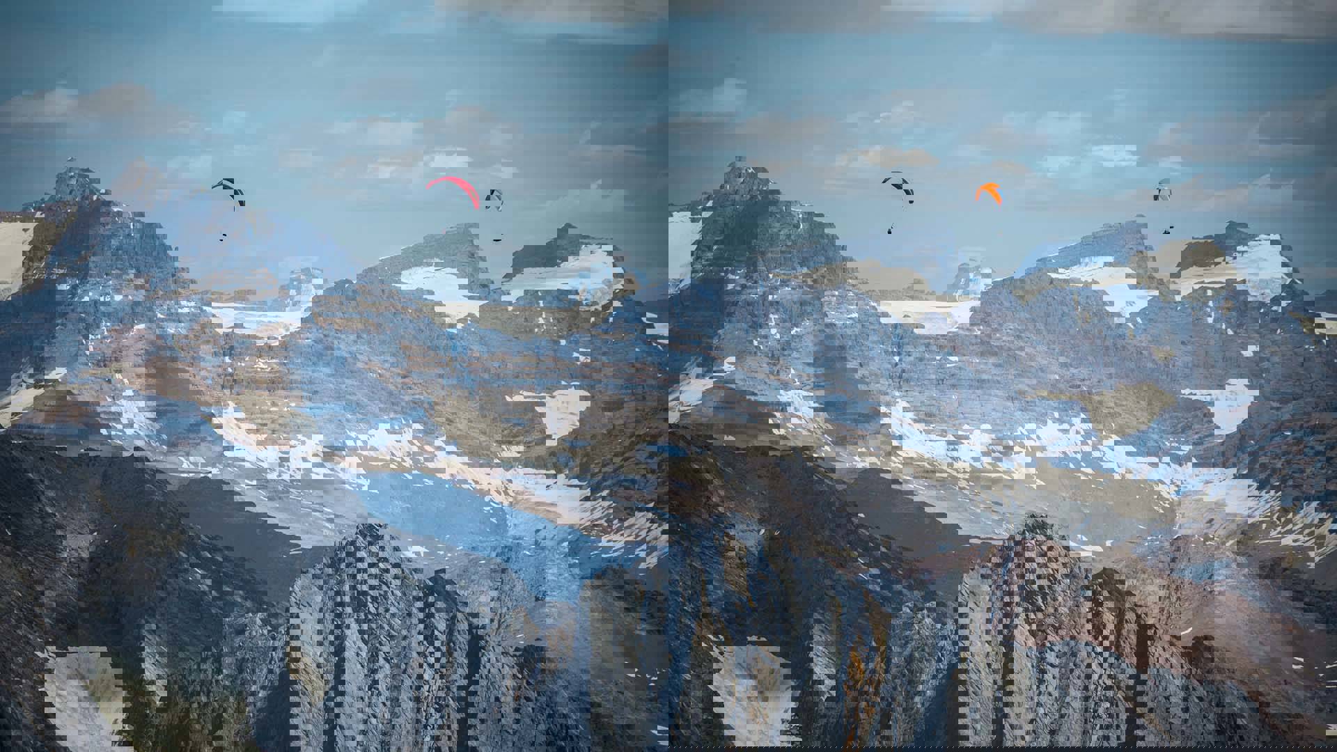 A landscape shot of two parachuters in the sky over the snowy Rockies mountains.