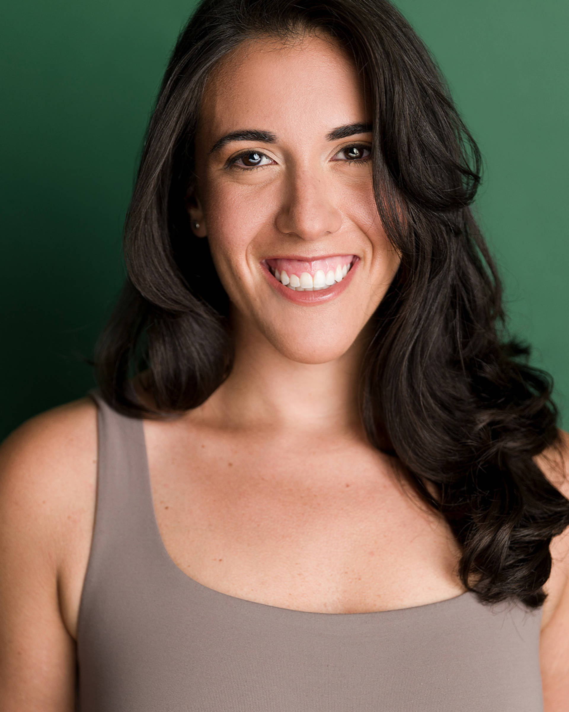 Headshot of a woman with light complexion, long dark hair, and brown eyes. She is wearing a tan top.