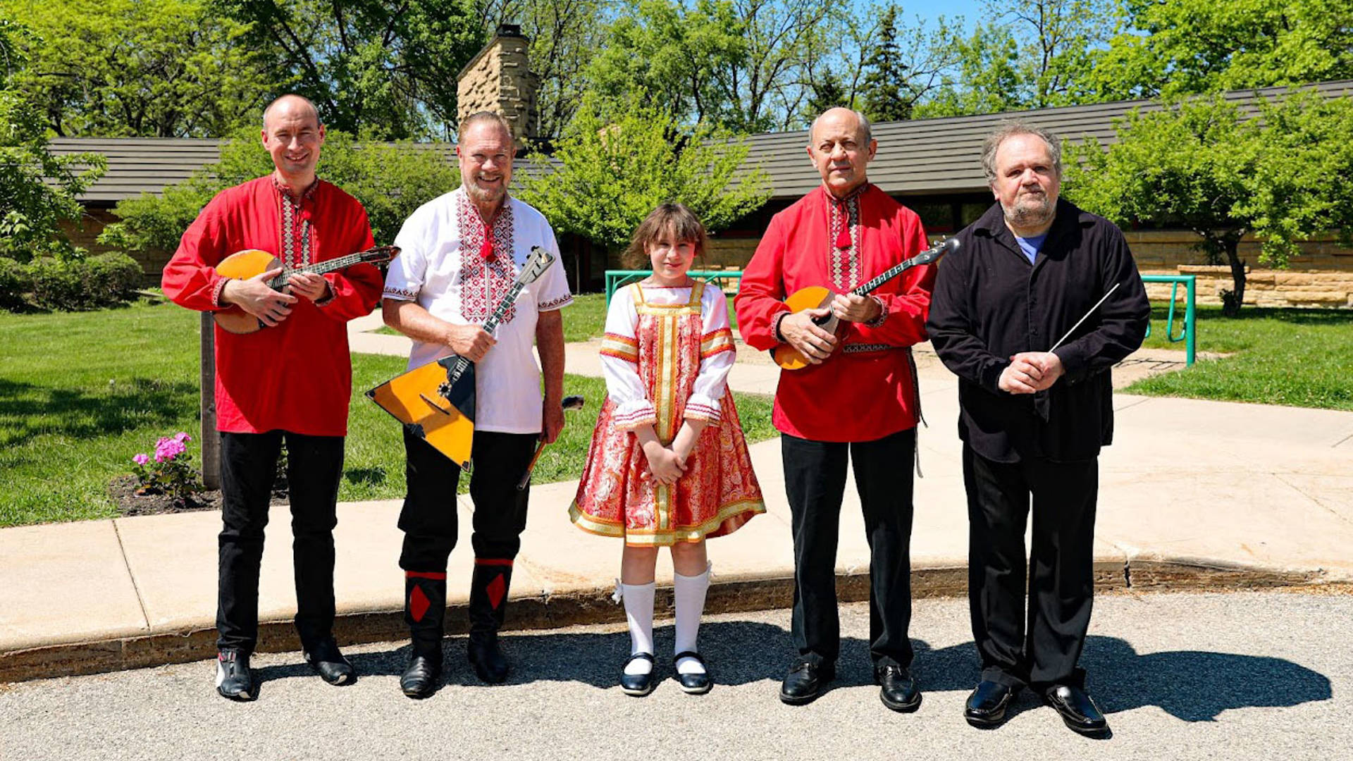 Five people standing outside in traditional russian outfits and holding russian folk instruments