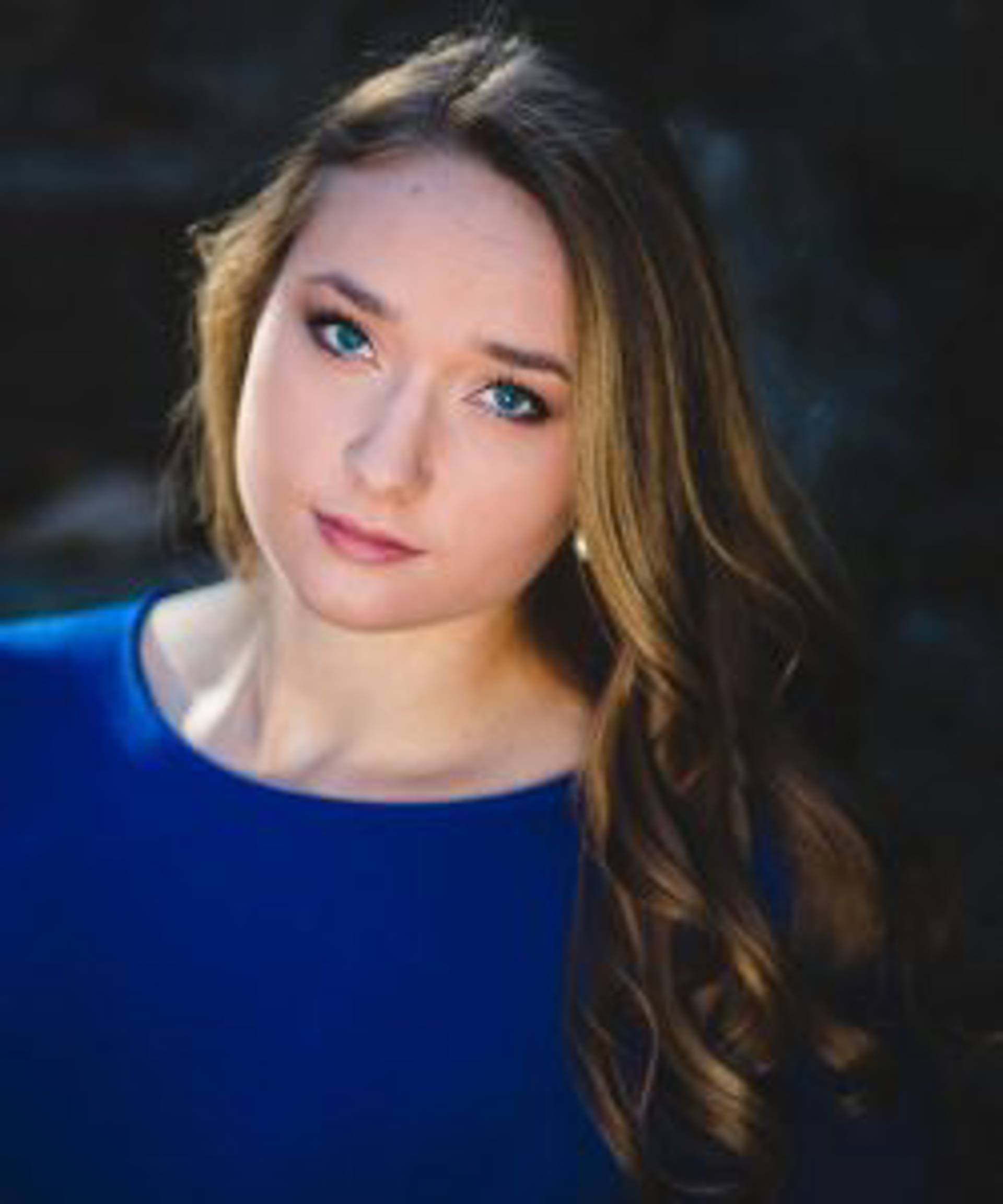Headshot of a caucasian woman with blond hair and blue eyes in a blue dress.
