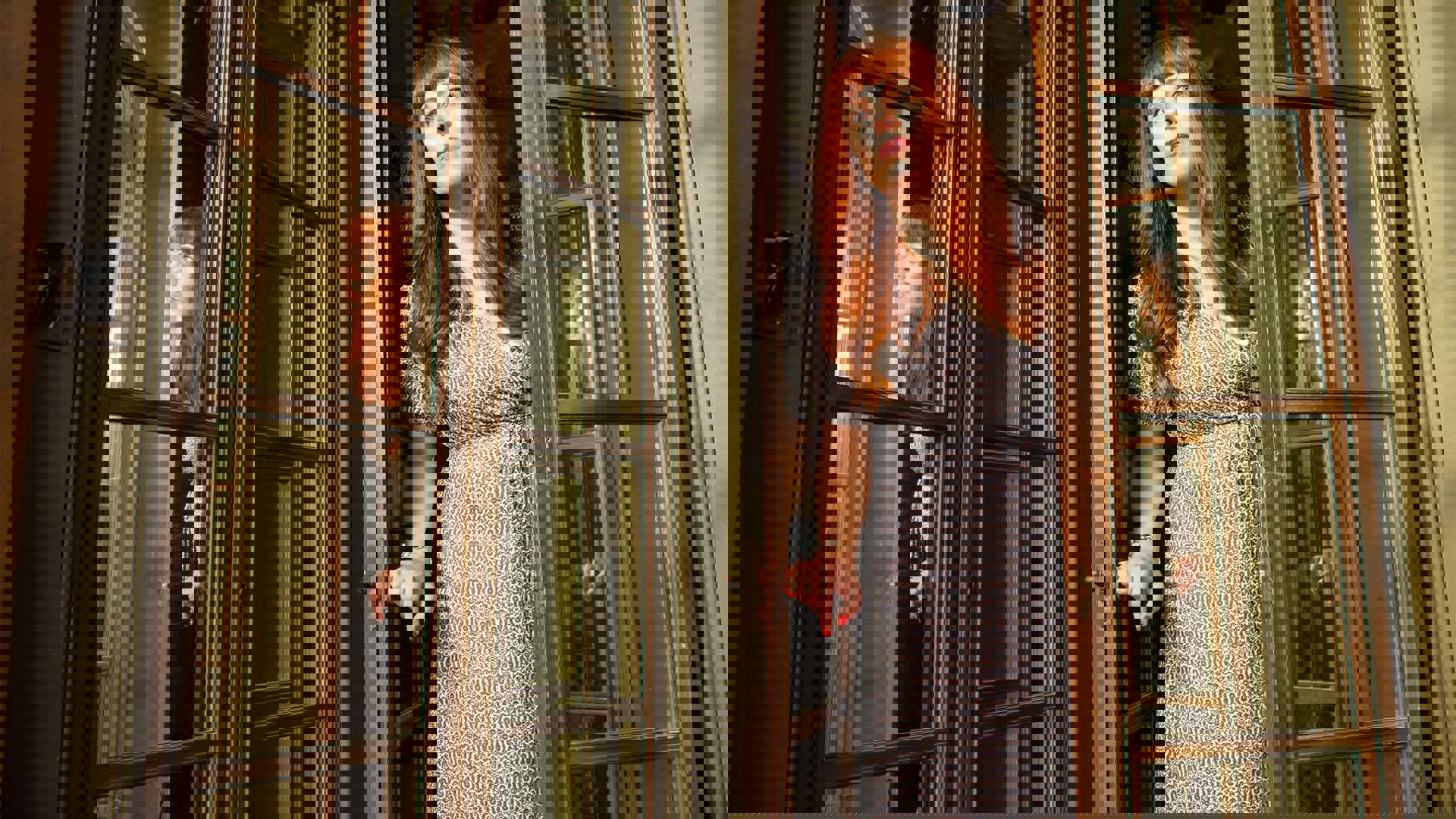 A white woman with reddish-brown, shoulder-length hair opening a class door and looking curiously into a room. 