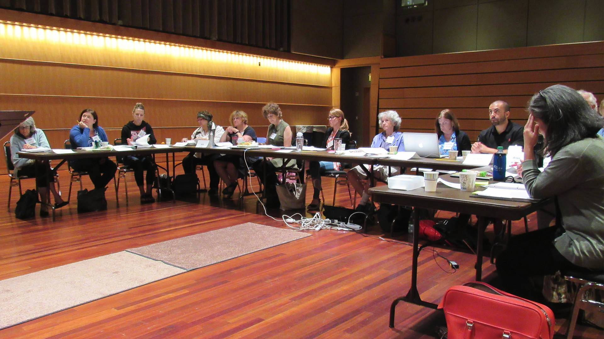 A group of adults sitting at a table in a U-shape watching a presentation.