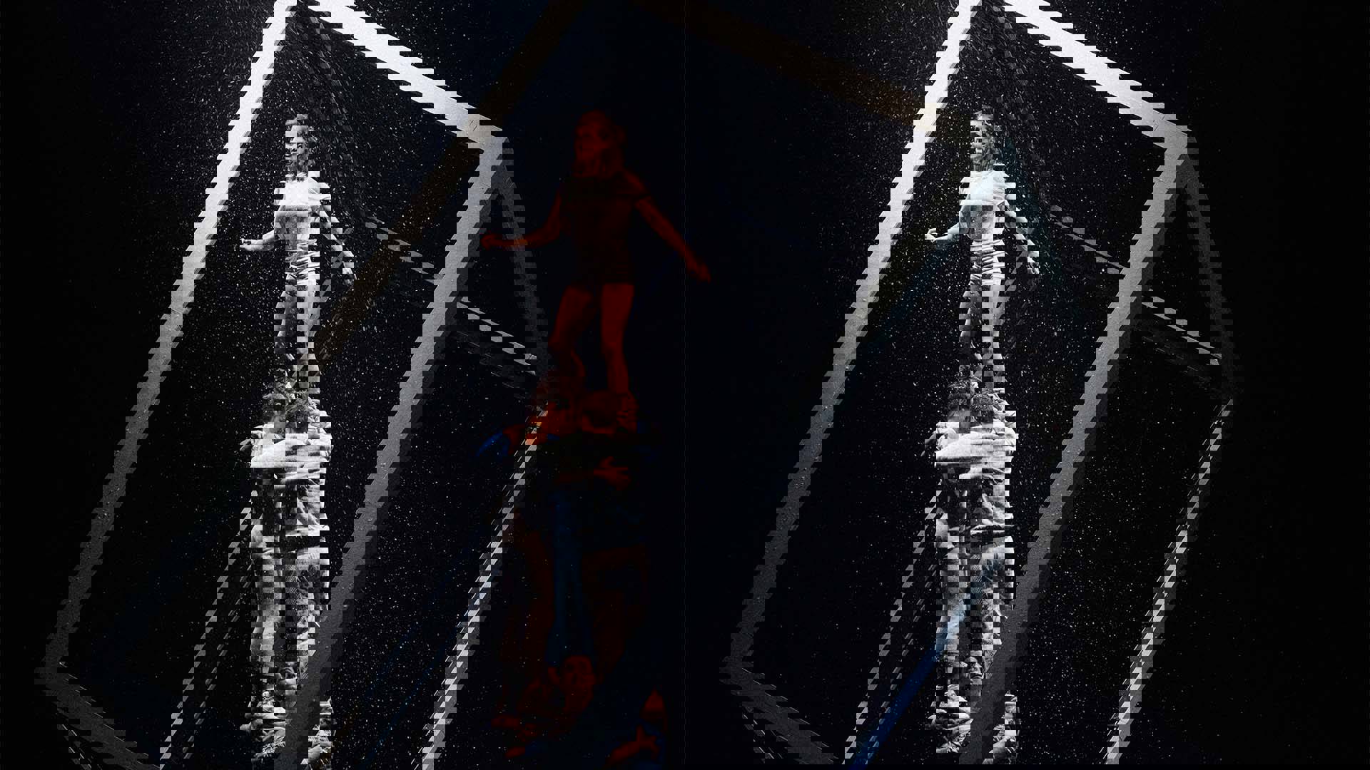 A group of dancers forming a human pyramid with one dancer at the top. They are in a large framed box with snow falling down.