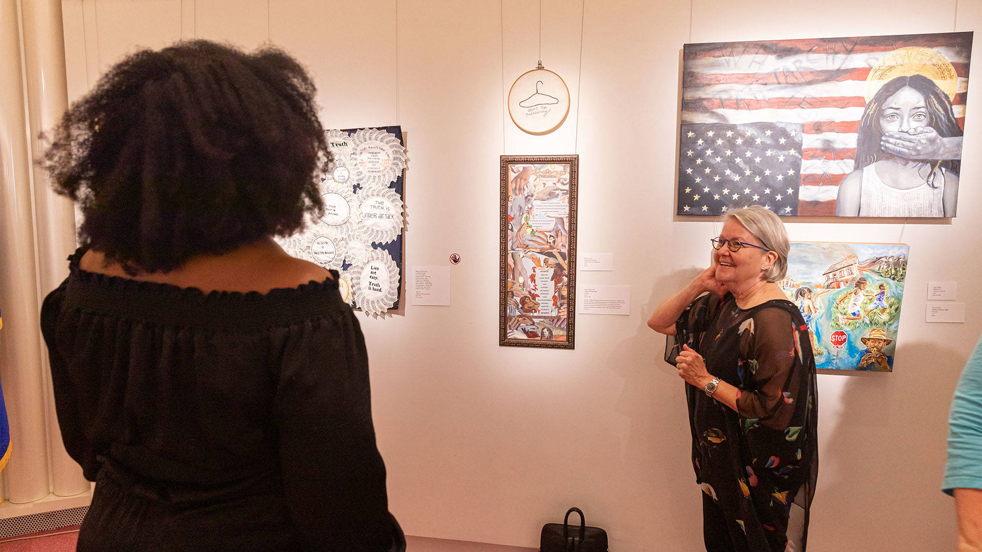Two people look at several pieces of art on a wall.