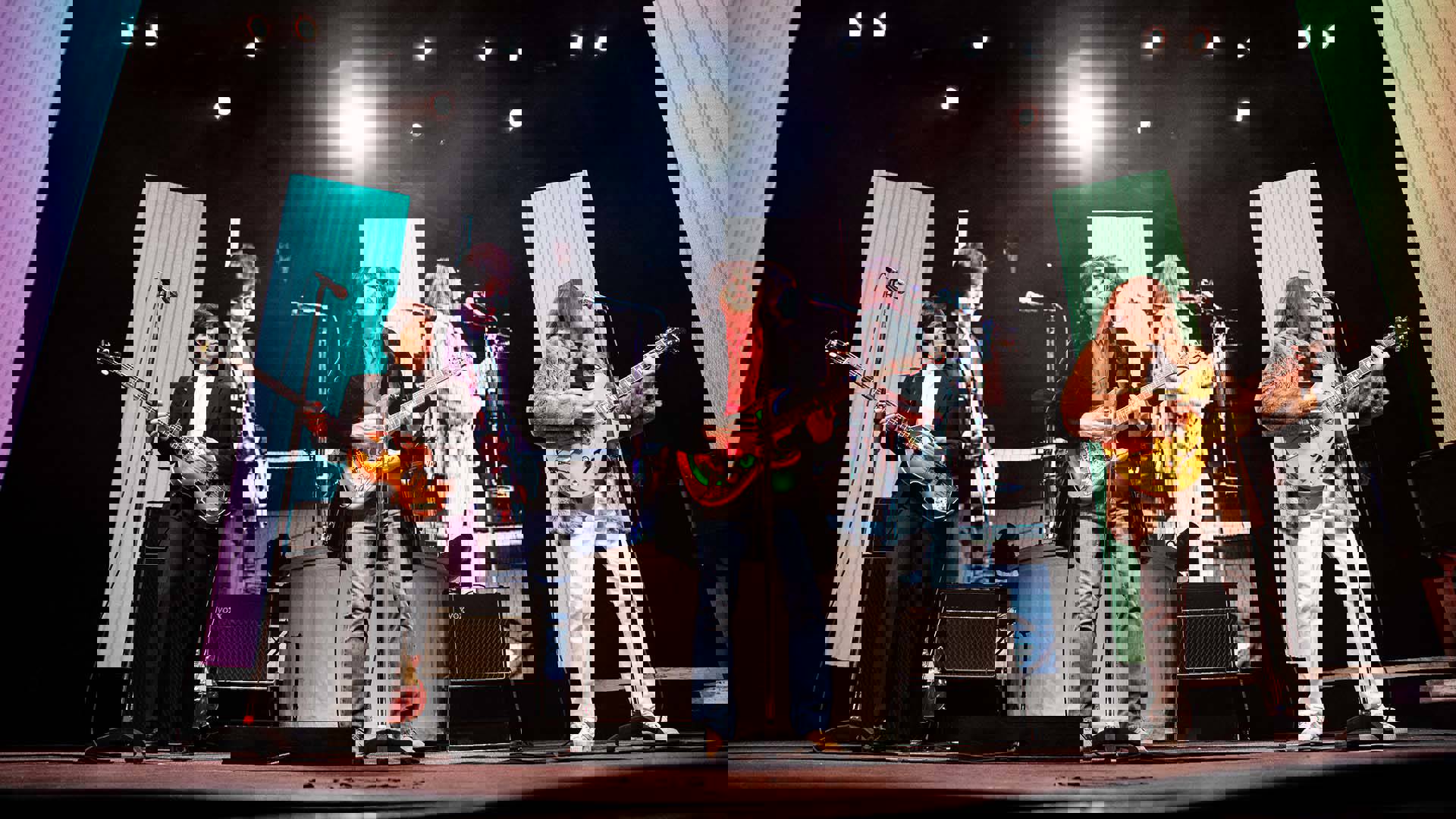 Four Beatles impersonators performing the "Rooftop concert" with guitars and stylish 1960s clothing