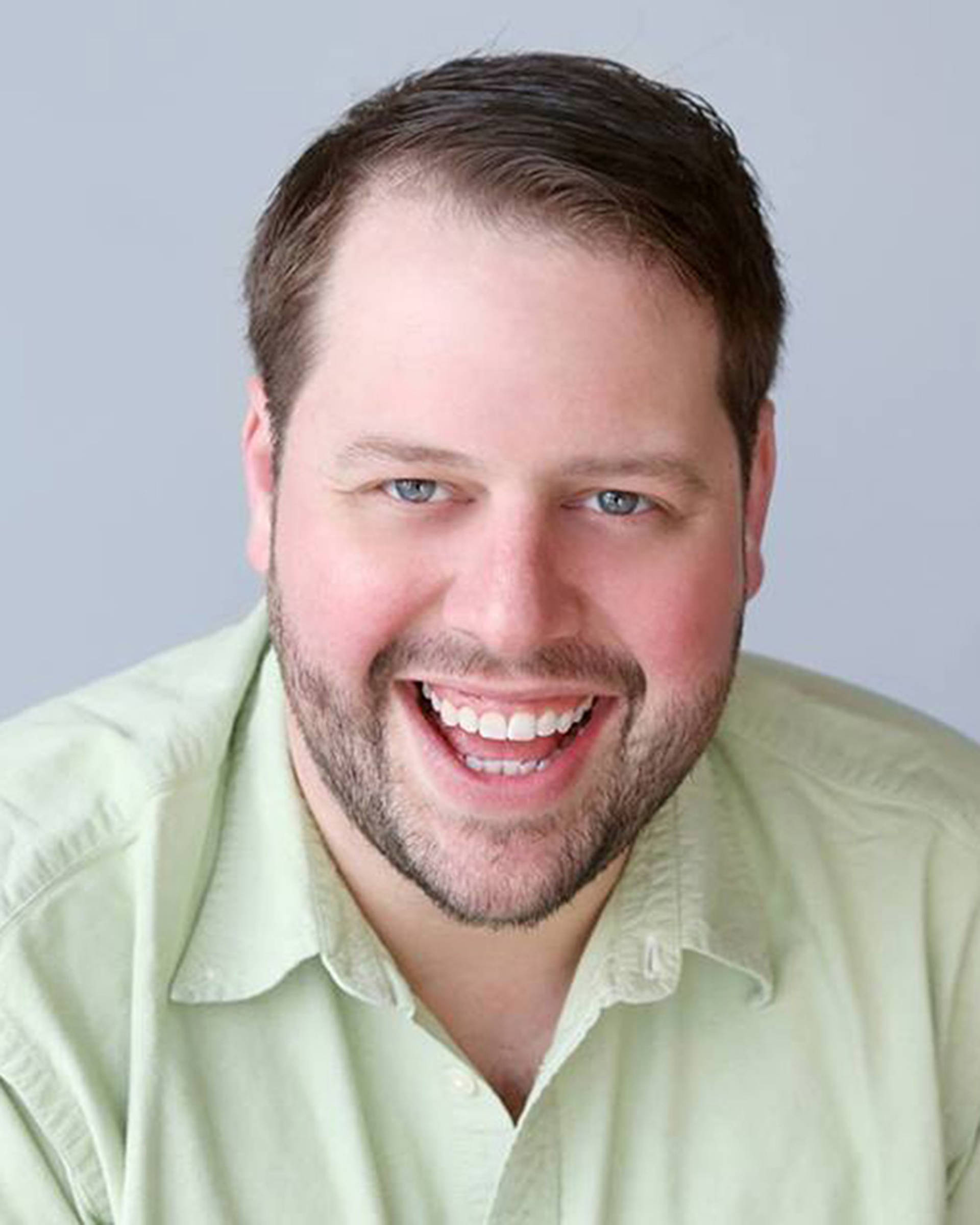 Headshot of a white man with short dark hair, blue grey eyes and five o'clock shadow