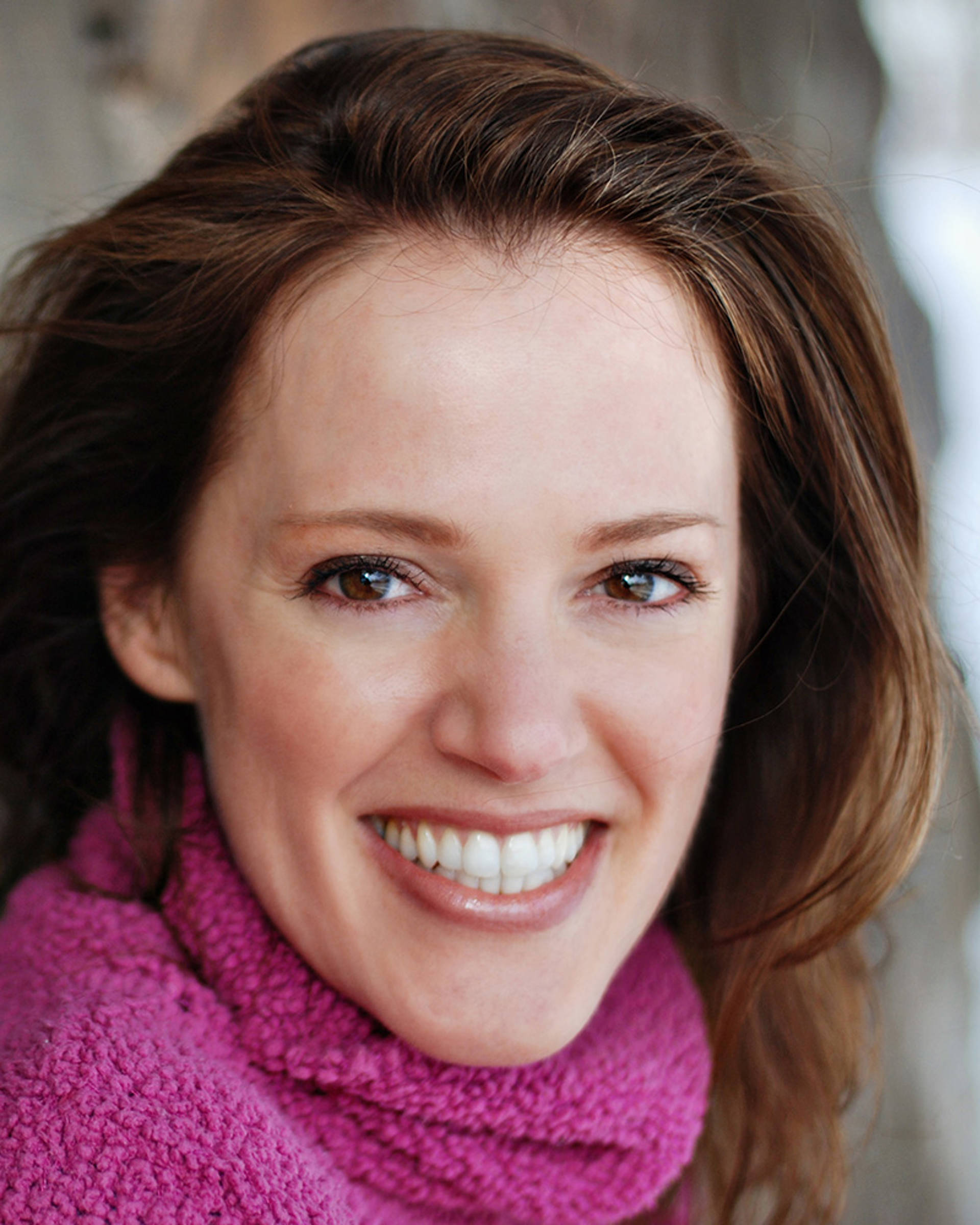 Headshot of a caucasian woman with long brown hair and brown eyes. She is smiling and wearing a pink sweater.