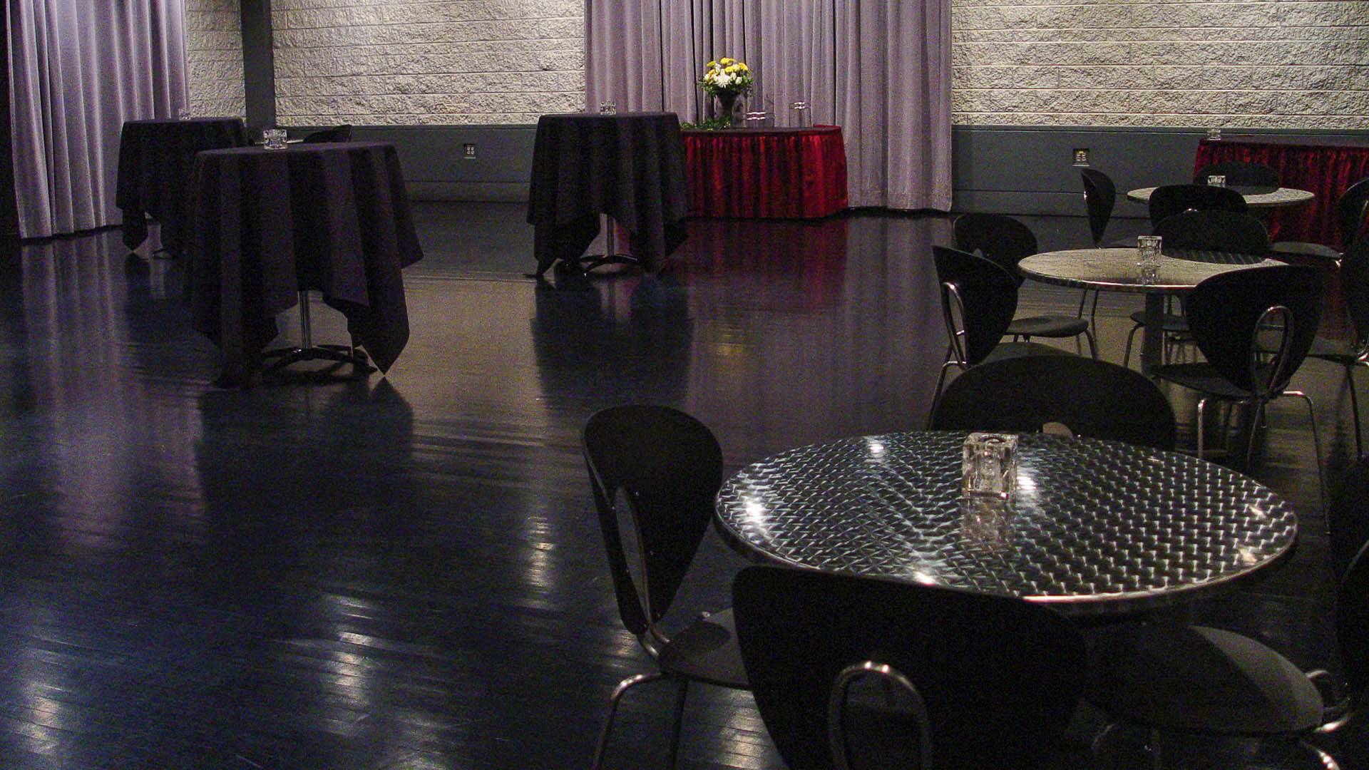 A space with black flooring and white brick walls. There are several round tables and chairs.