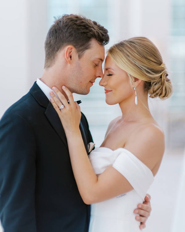 A white couple on their wedding day embrace with their eyes closed. the groom is touching the tip of his nose to the bride's.