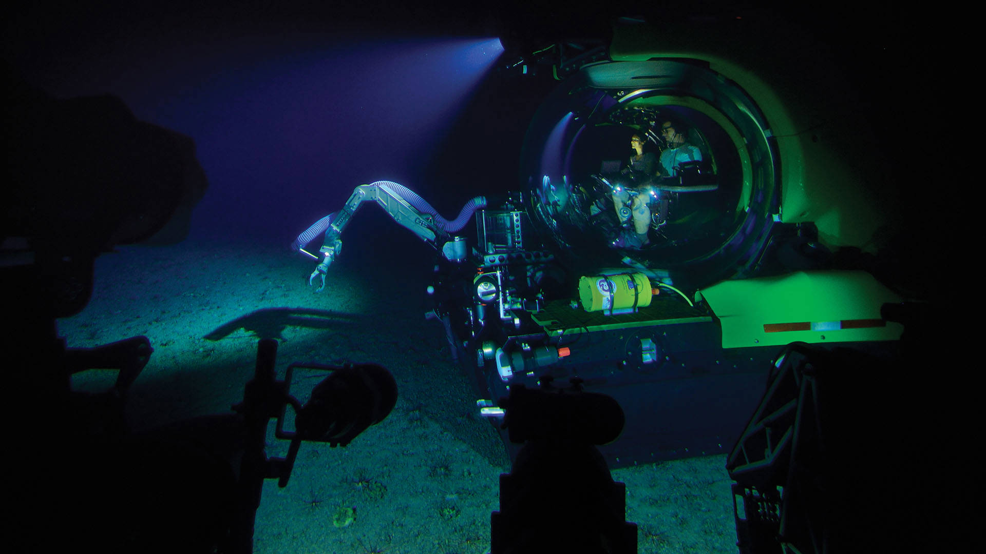 A yellow deep sea exploration vehicle with all sorts of tools and robotic arms. Inside a glass bubble at the center are two scientists