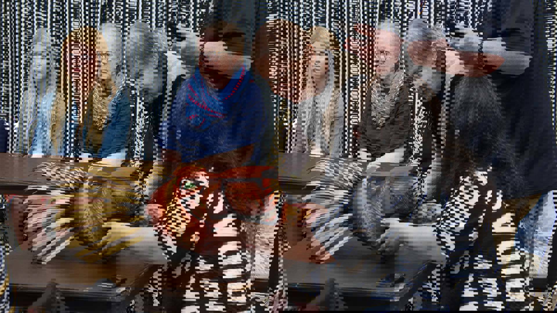 A wooden lion mask on a table. People are sitting around it and touching it.