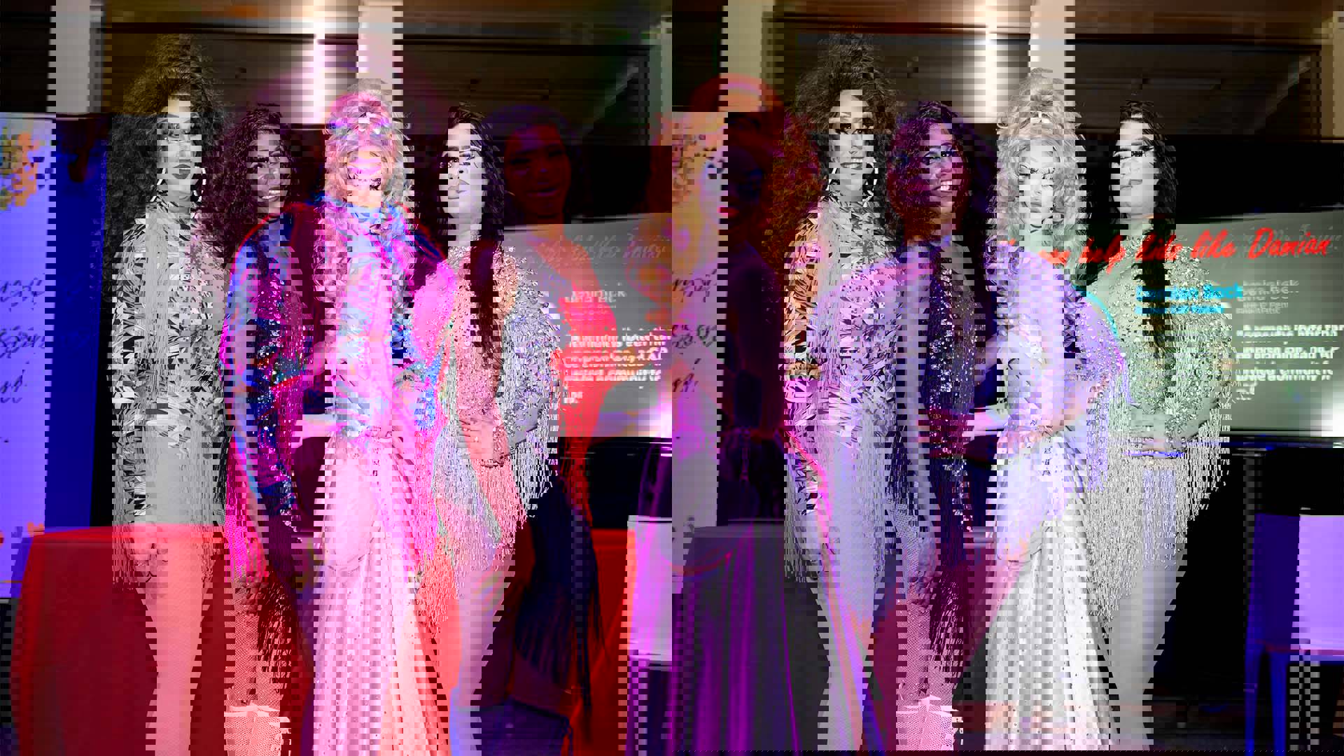 Four drag performers in colorful outfits pose together for a photo.
