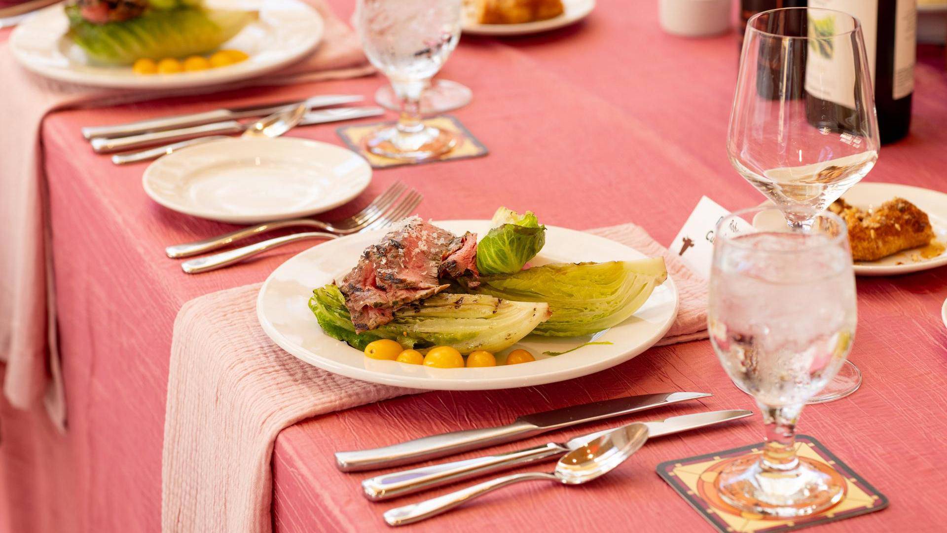 A plate of beef, tomatoes, and leafy greens on a fancy dressed table.