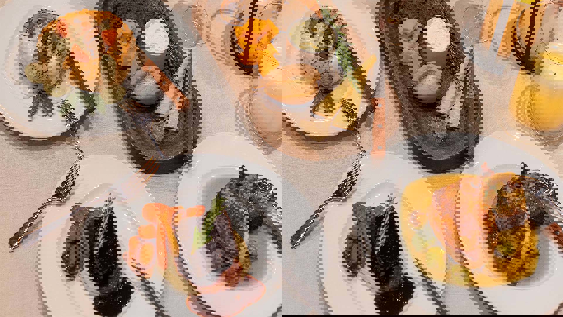 A linen table setting with lit candles and three plates of rustic entrees, including a vegetable pot pie, beef and chicken, with a wood board of bread and cheese.