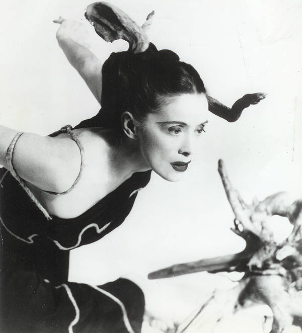 Black and white photo of a young Martha Graham striking a dance pose in a black dress and makeup.