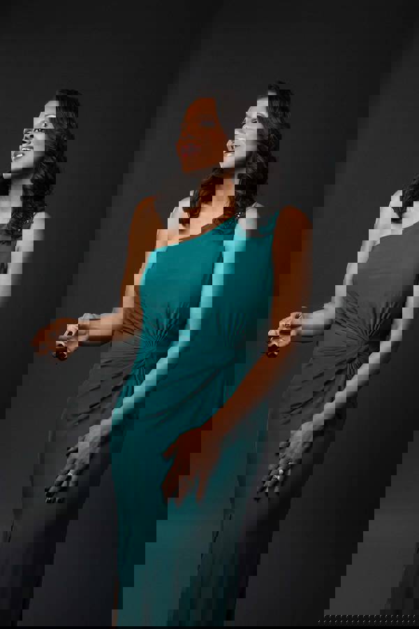 Audra McDonald, a woman with dark brown hair and a dark complexion, wears a teal dress and poses for the camera.