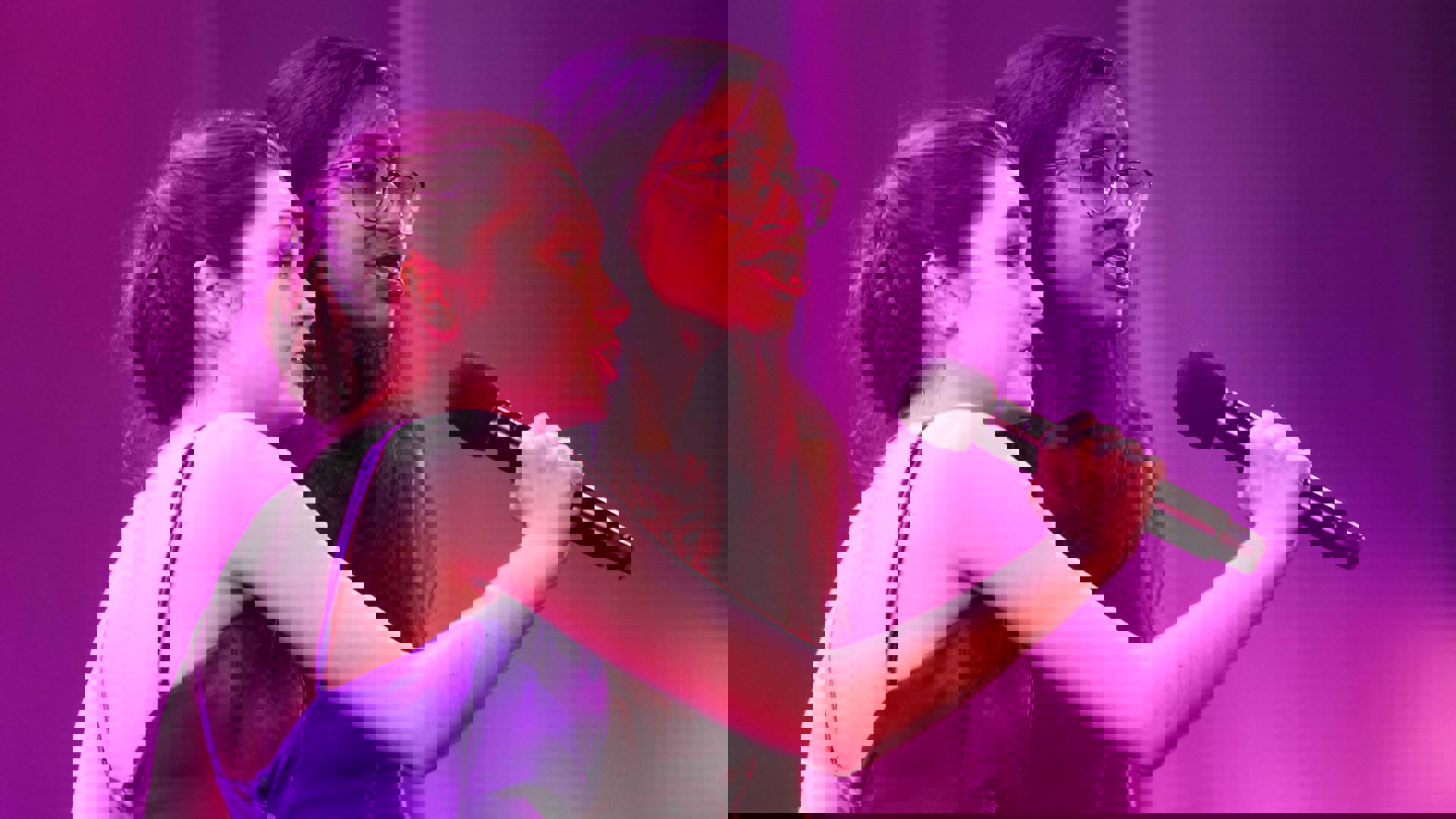 Two young women singing into a handheld mic.