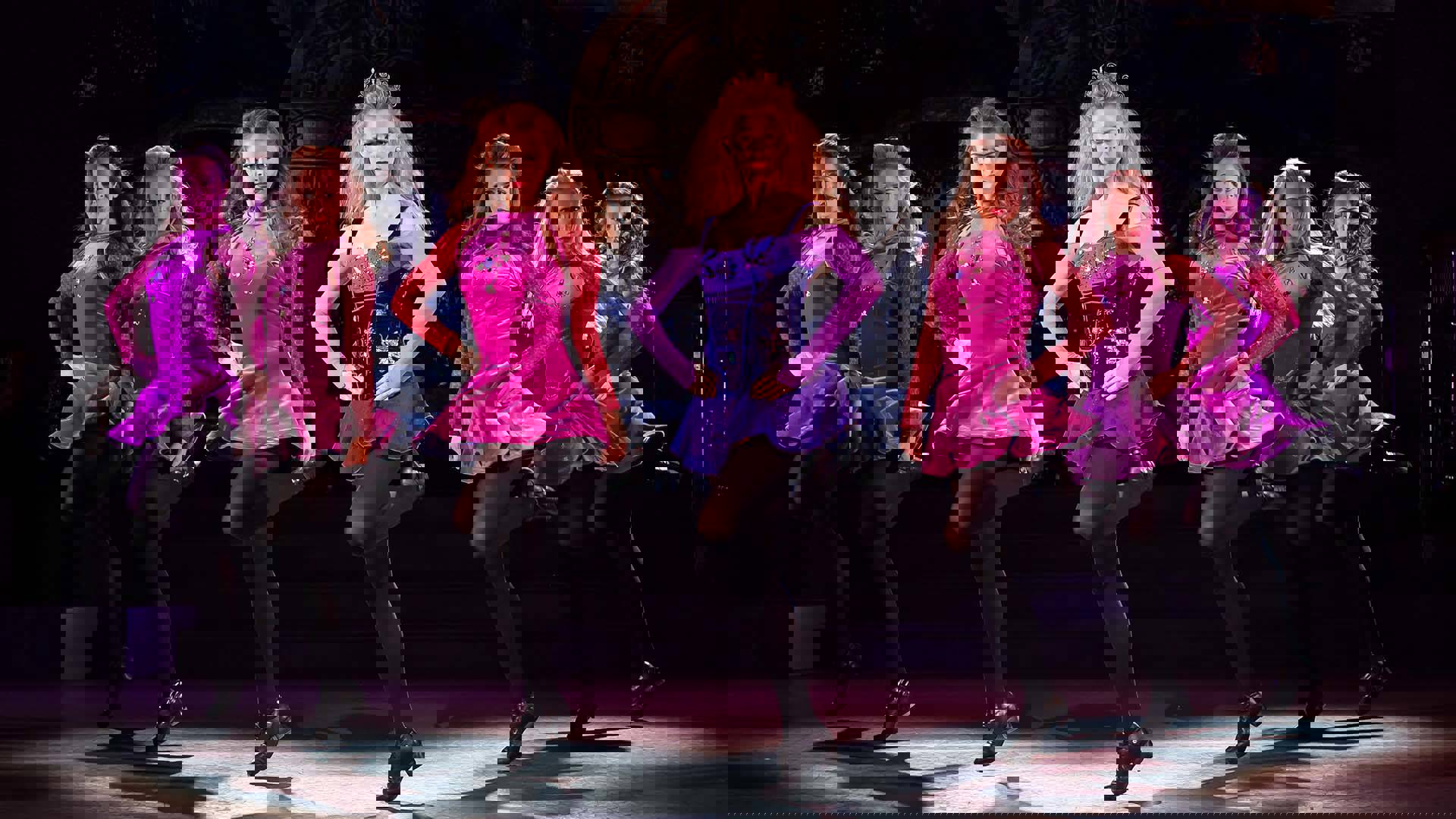 Seven dancers with light complexion and long blonde and brunette hair, Irish dance with black tap shoes and pink and purple velvet dresses with short skits.