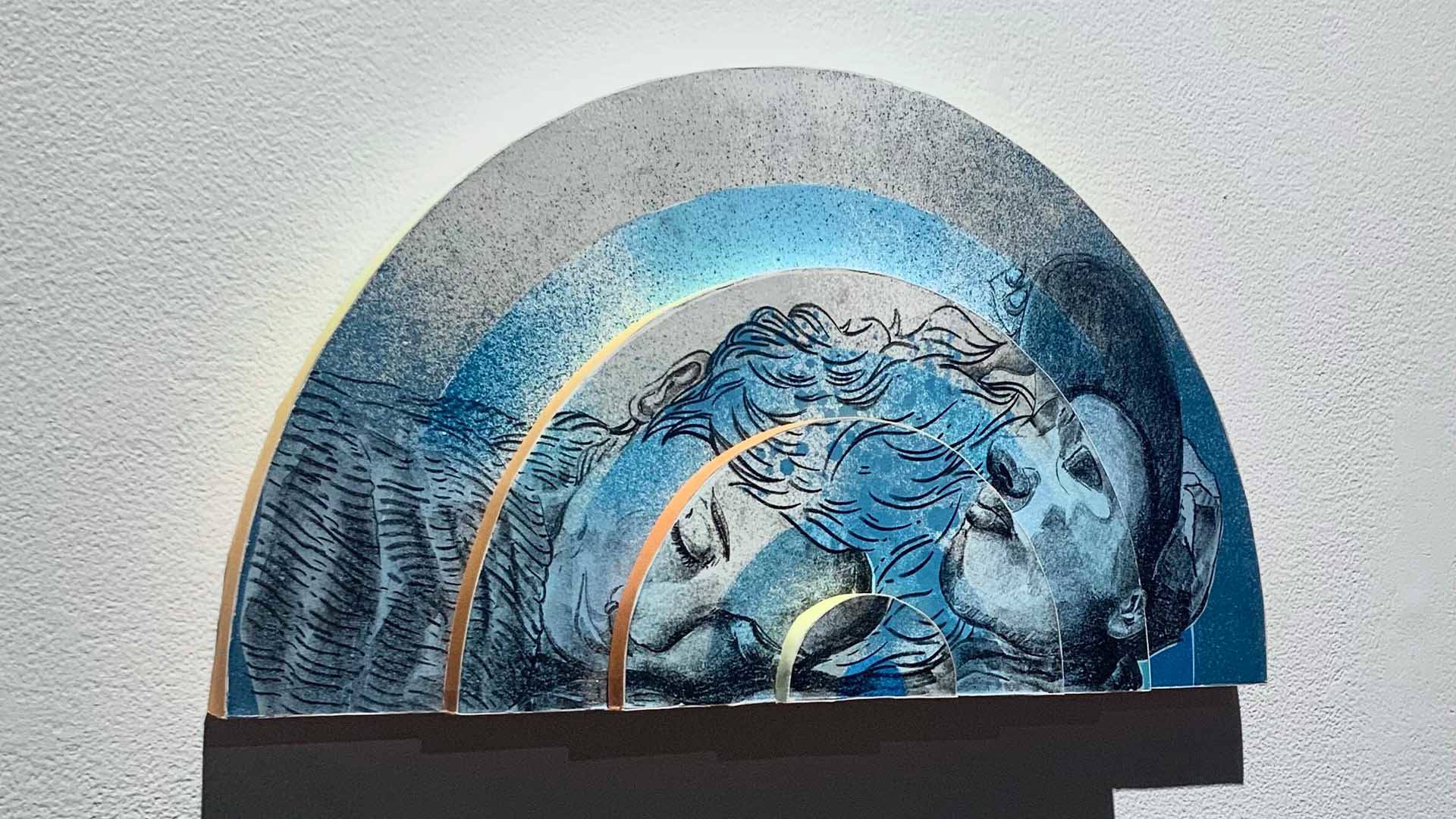 A piece of art in the shape of an arch. It is blue and grey and features a woman sleeping and a man with a baseball cap.