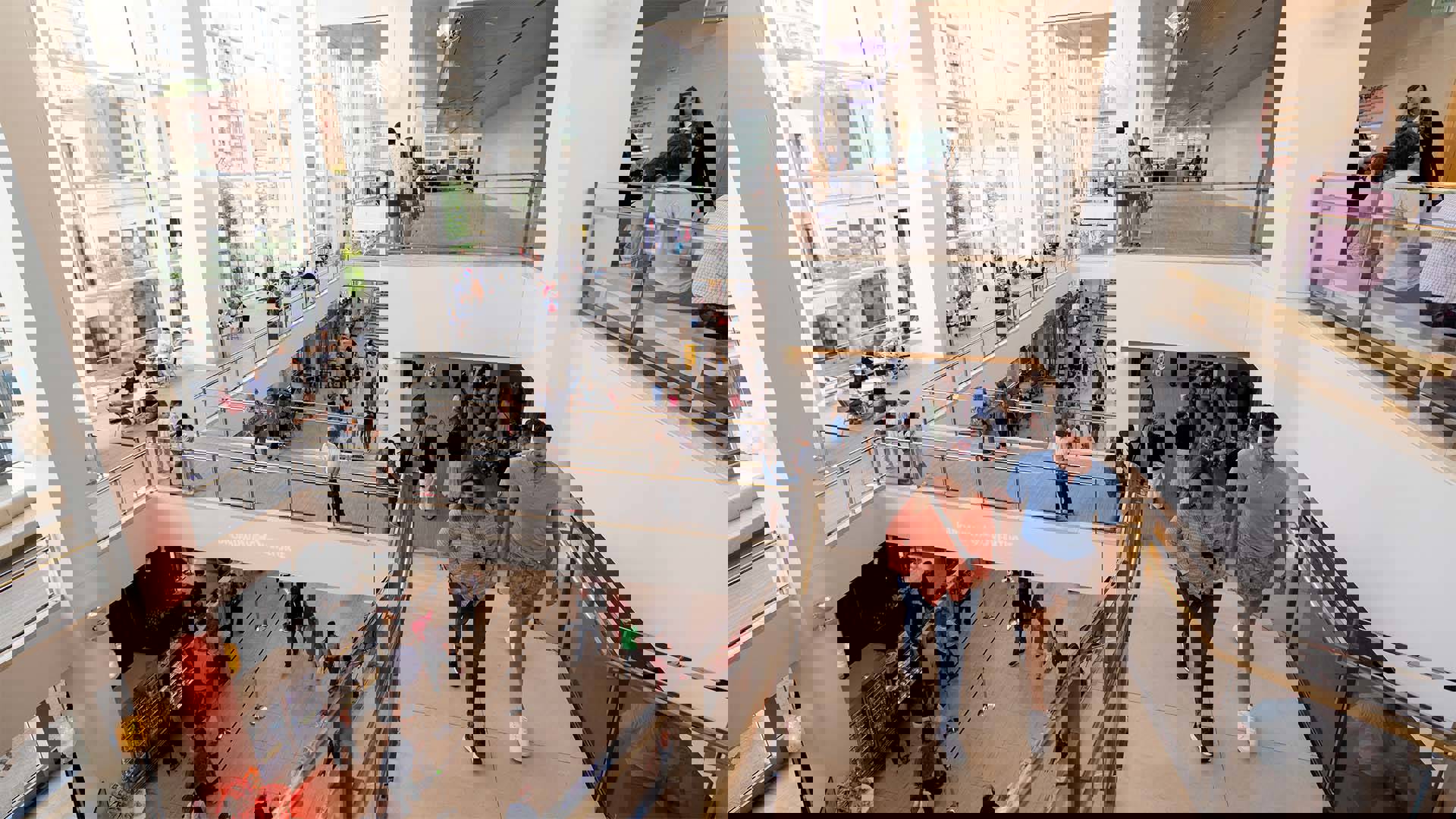 High view of Overture Hall Main Lobby, a large room with a rightside wall of windows facing Madison's downtown. People are crowded on the floor below in lines for concessions.