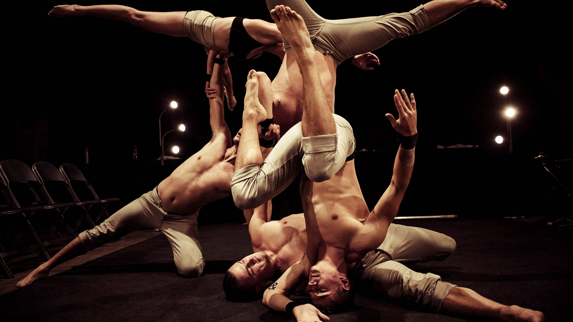 A group of dancers in minimal tan clothing contort and knot up their bodies in performance