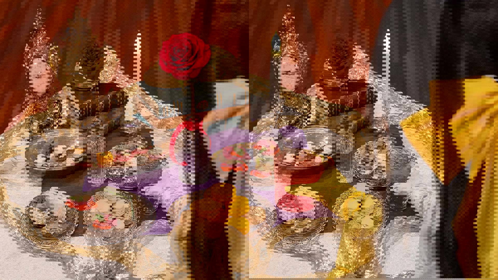 A woman with dark hair with a yellow bow holds a cup of red punch while looking at a table filled with finger sandwiches and macarons.