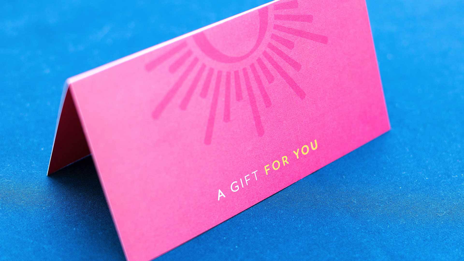 A pink card sitting on a blue table cloth. The card reads " A gift for you" and has the Overture Center logo on it as well.