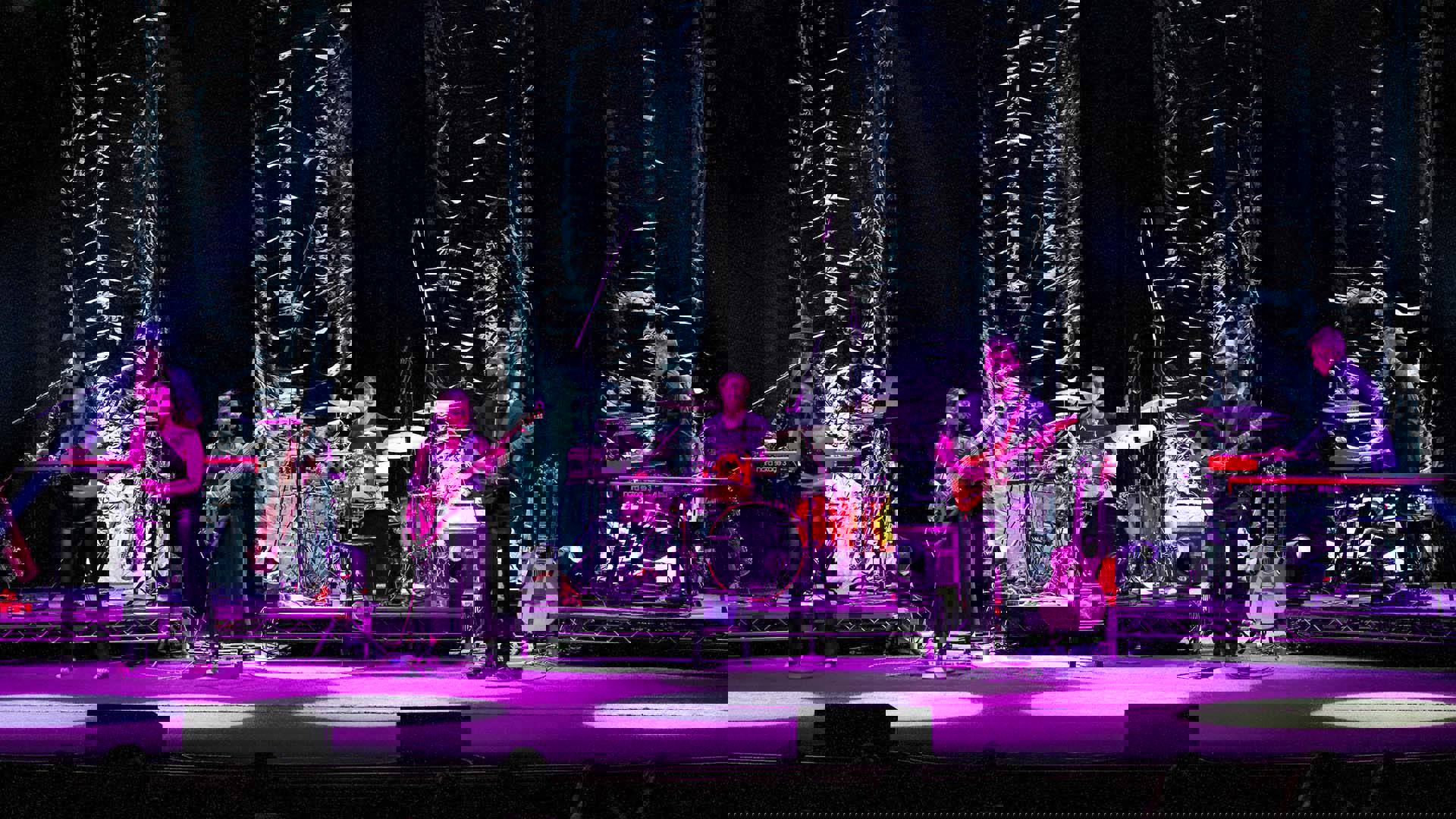 A band performing on a stage under purple lights.