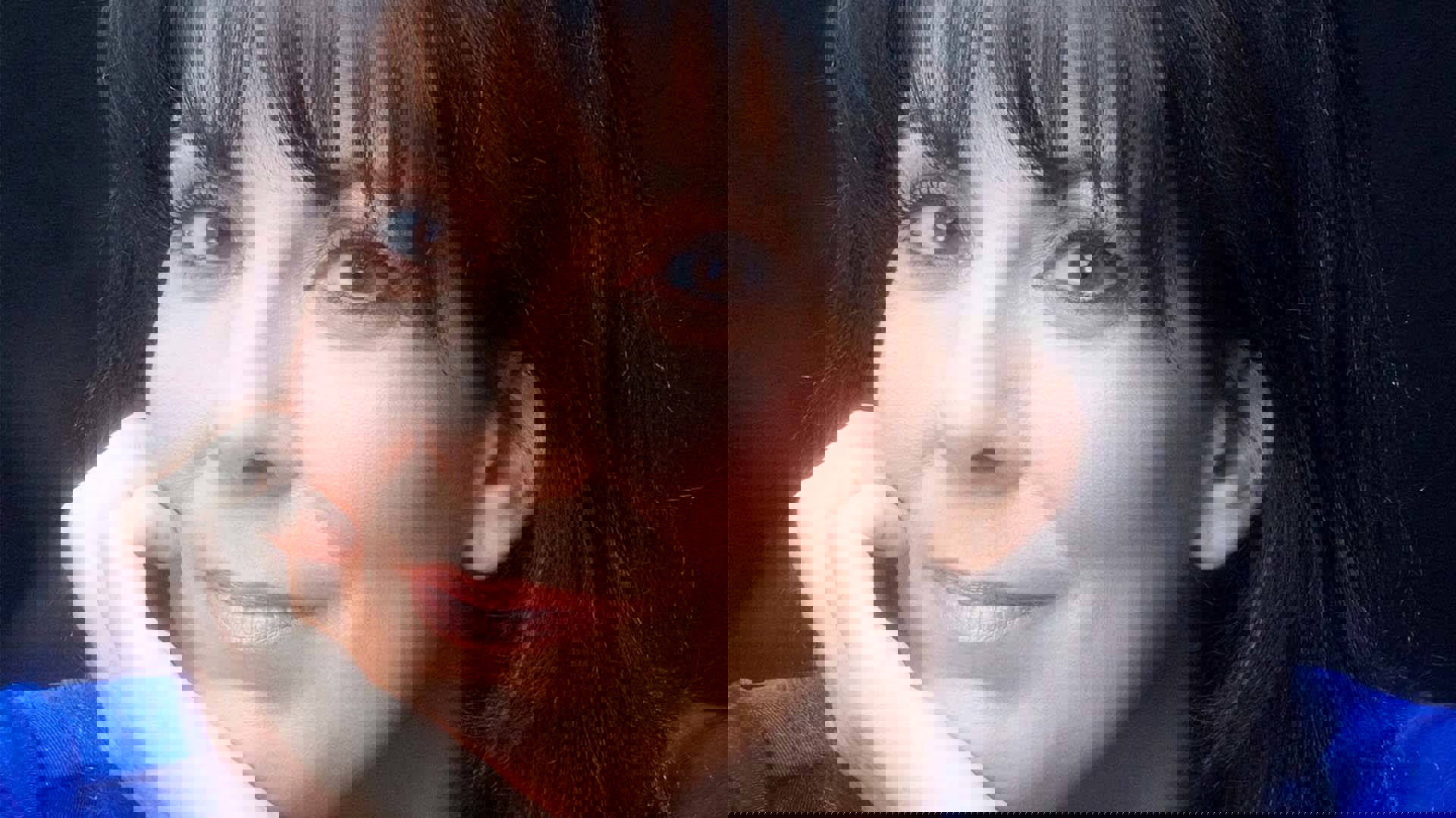 Close up of a smiling Christine Pedi as she rests her head on her right hand. She has brown eyes and dark hair.