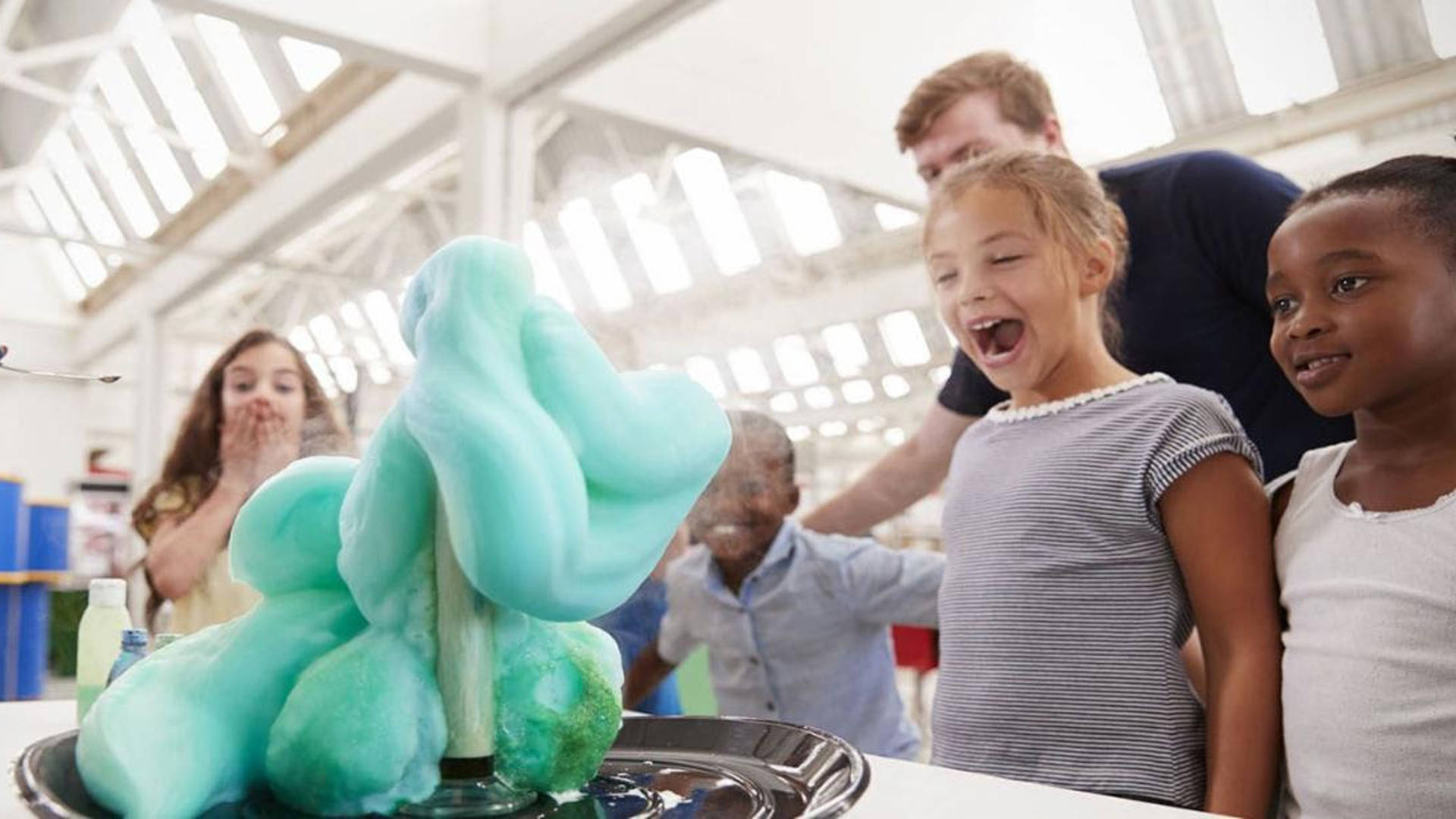 Children smiling and laughing as colorful foam pours from a cylinder.