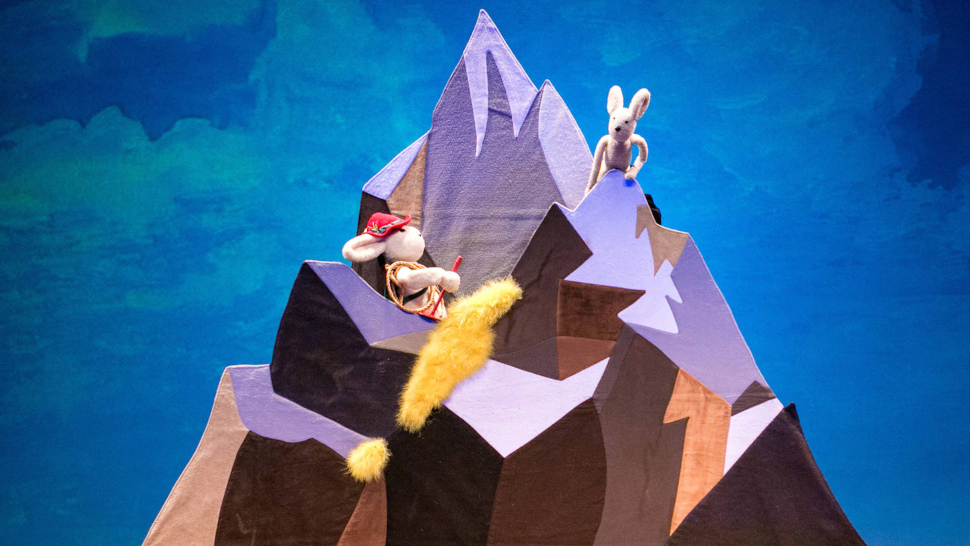 A puppet show displaying a winter mountain and two white rabbit puppets scaling the mountain side.