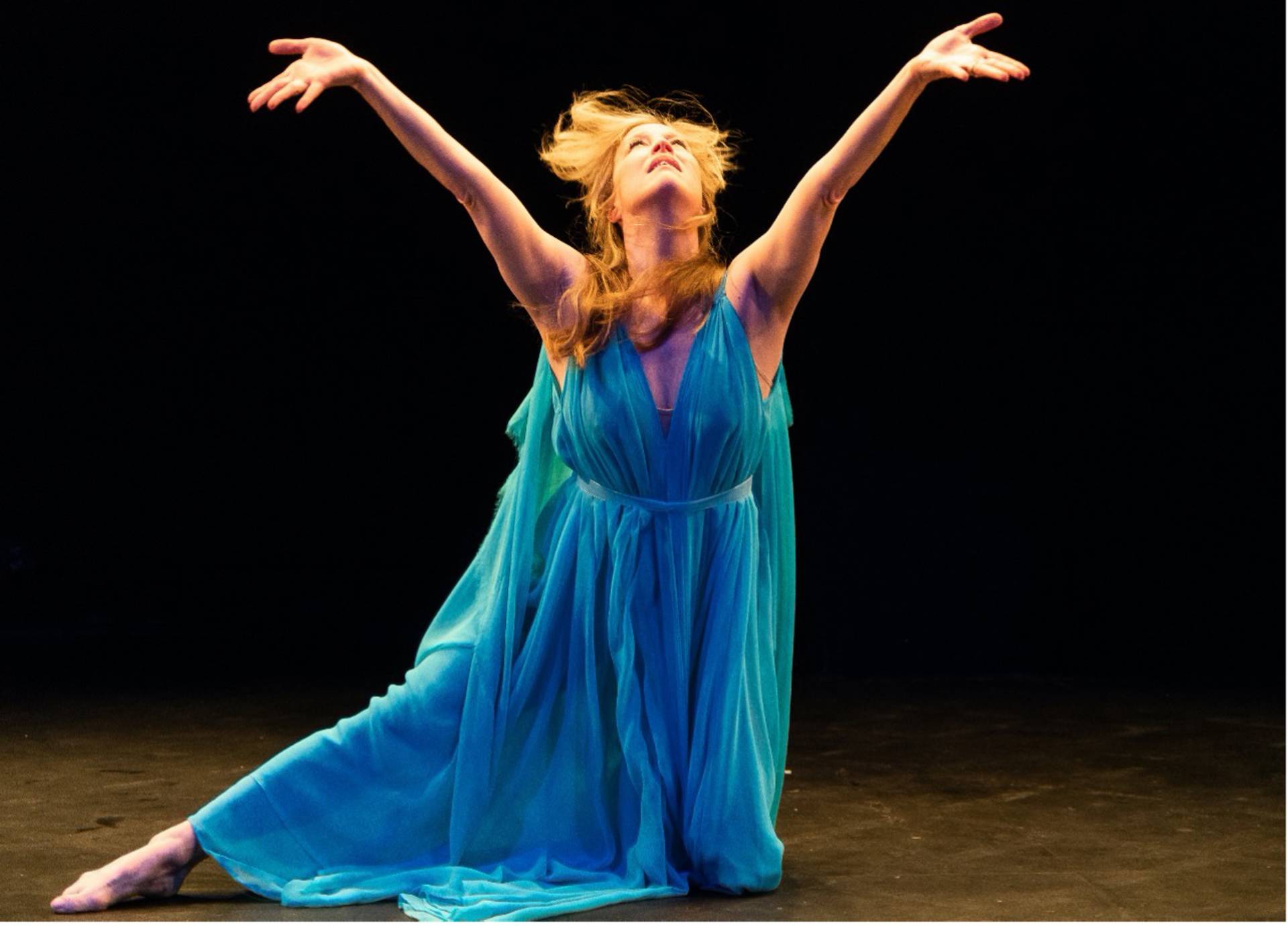 A woman dancing in a flowing blue dress. She has light skin tone and blond hair.