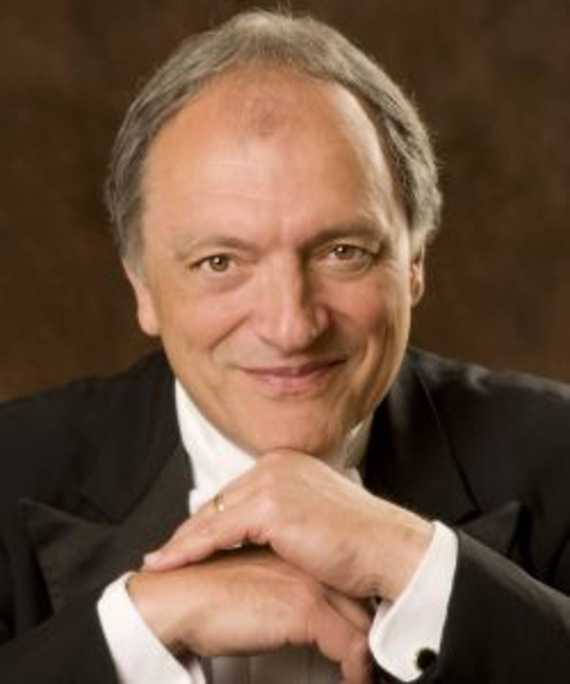 Headshot of a caucasian man resting his head on his hands and smiling. Hey has short grey hair and brown eyes.