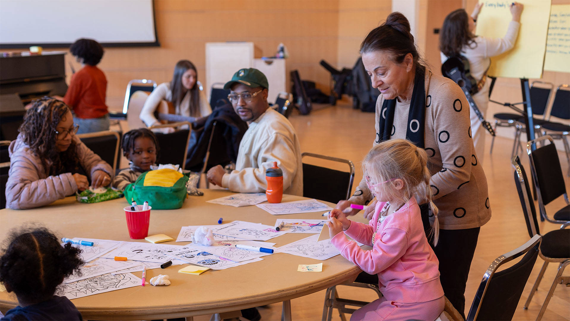 A child in pink clothing colors at a table while an adult helps.