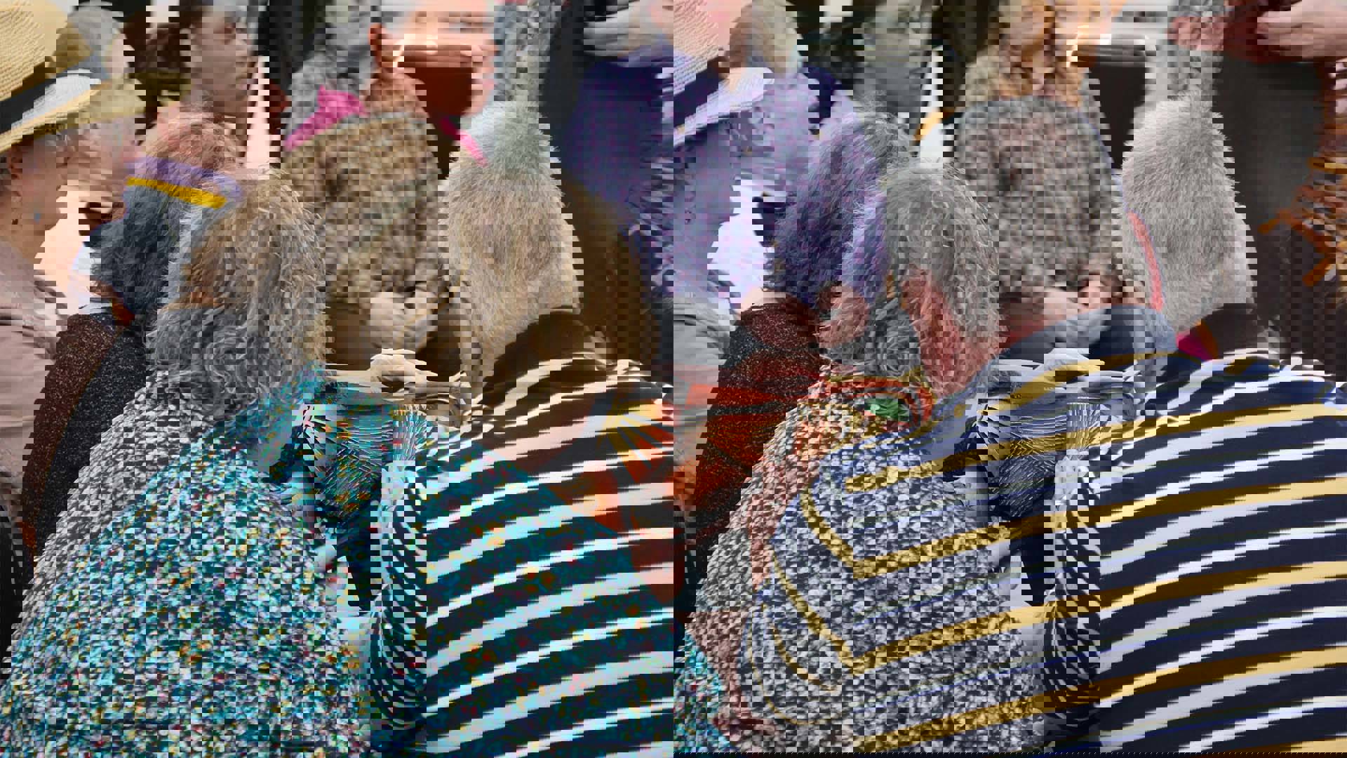 A wooden lion mask on a table. People are sitting around it and touching it.