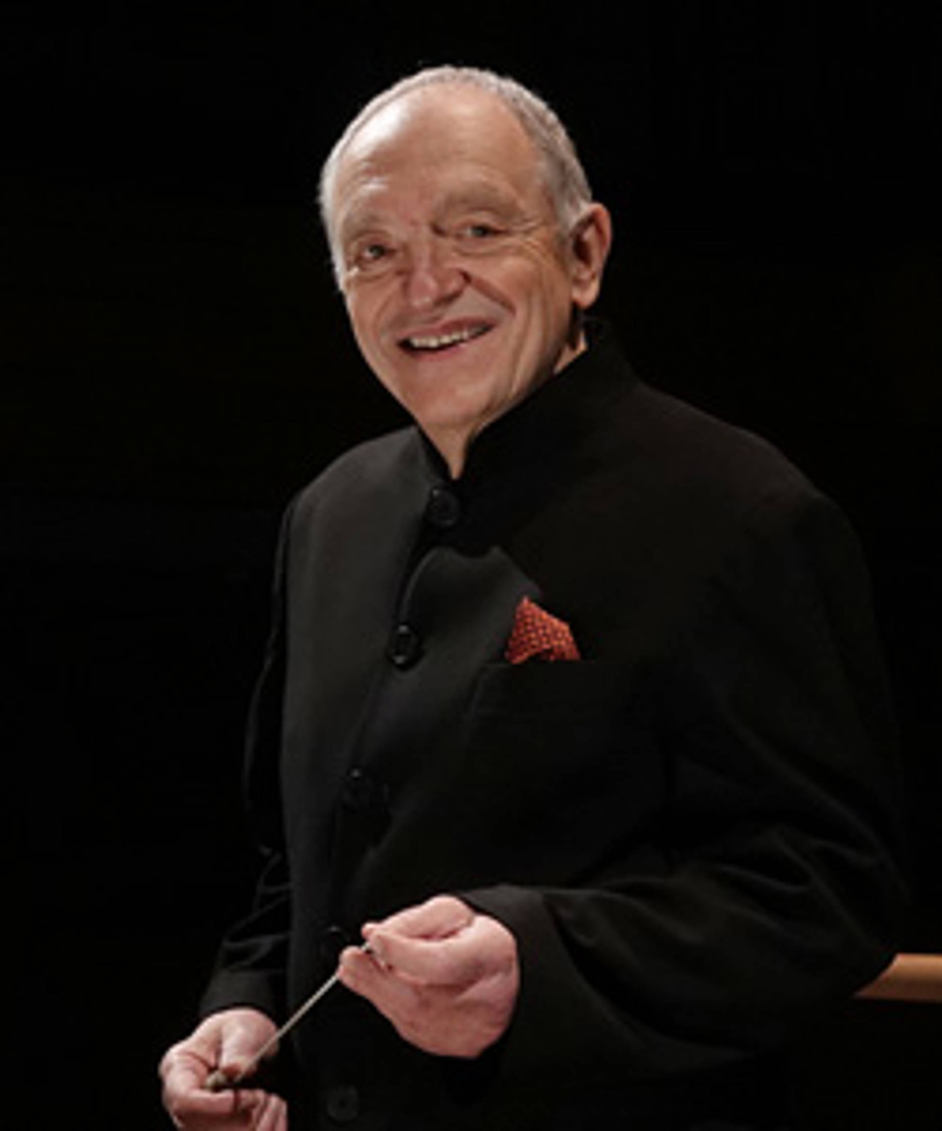 Headshot of a caucasian man holding a baton and smiling. Hey has short grey hair