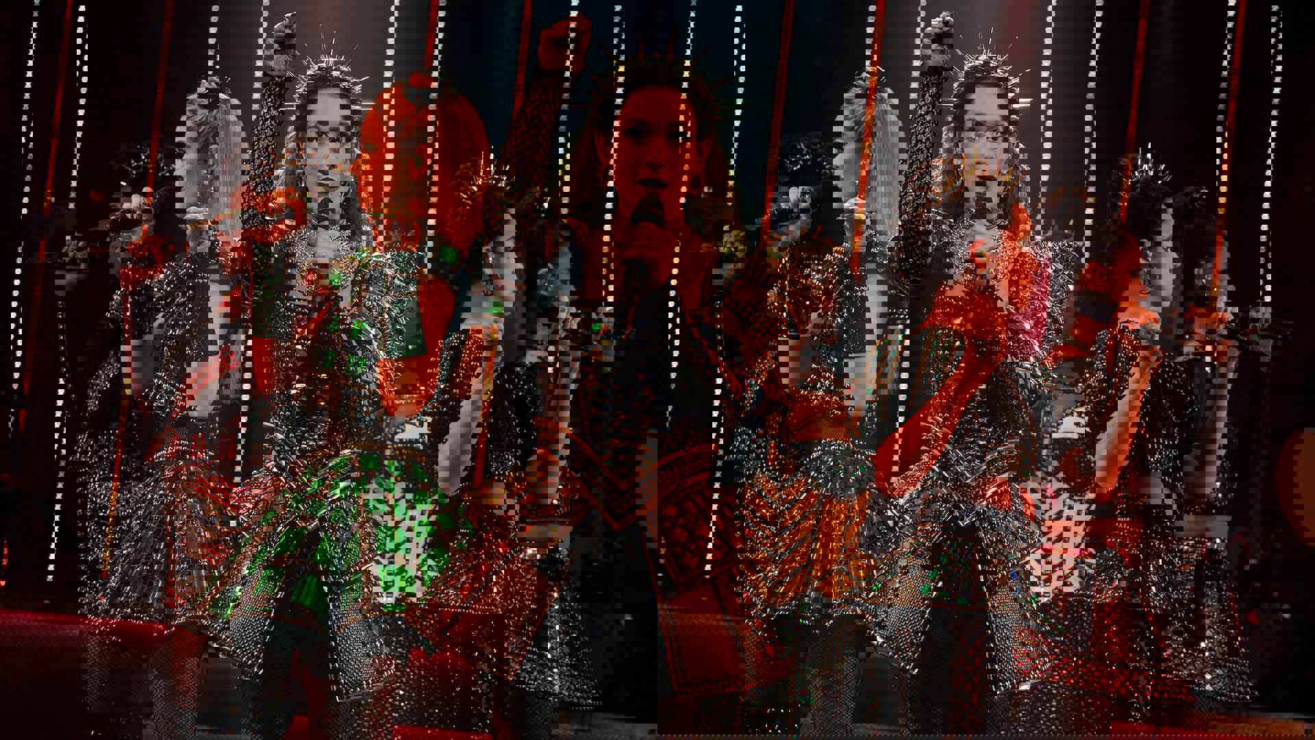 The cast of Six, in futuristic glittery outfits and holding microphones, performing on stage